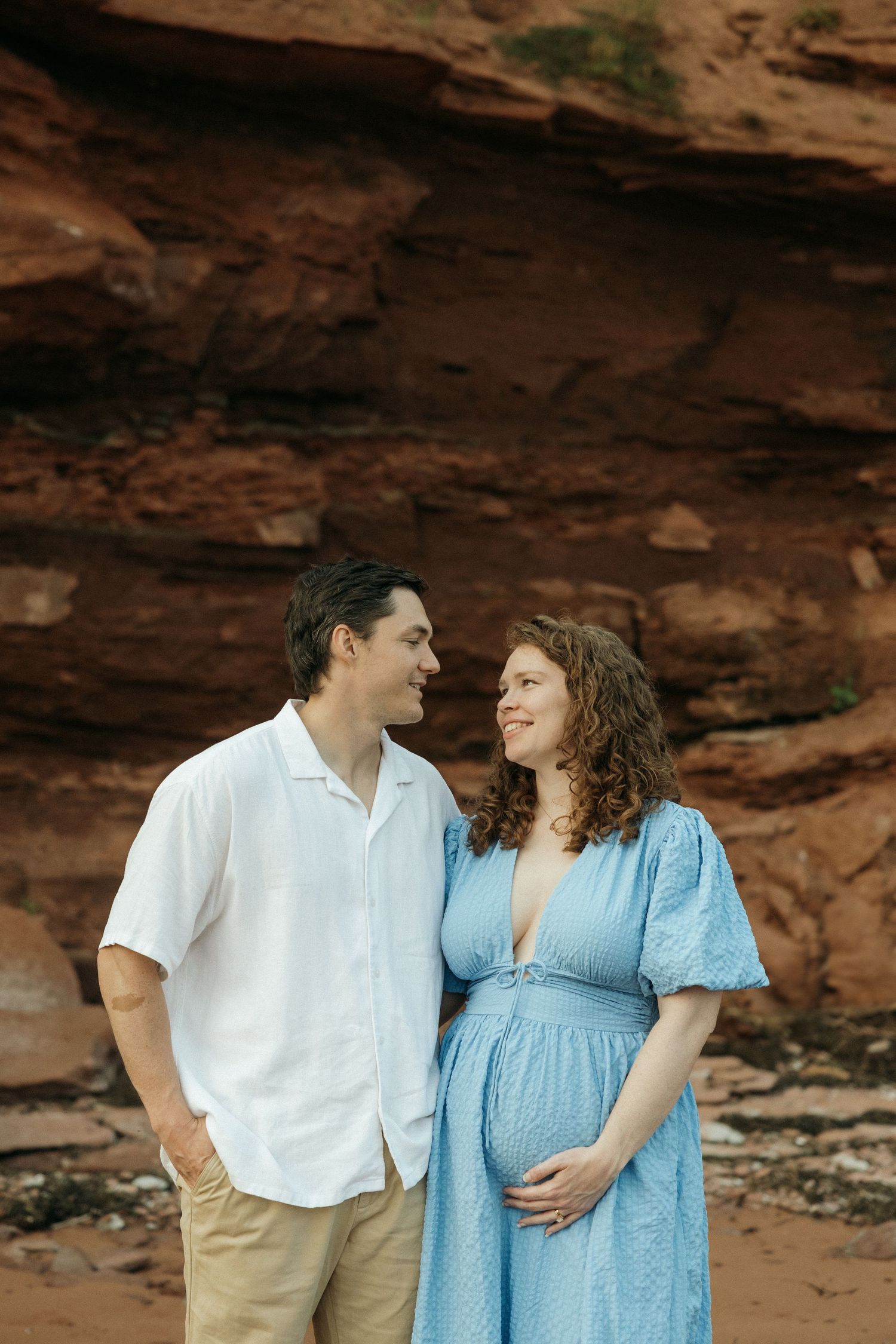 A maternity photo captures a couple in coordinated outfits against dramatic coastal cliffs.