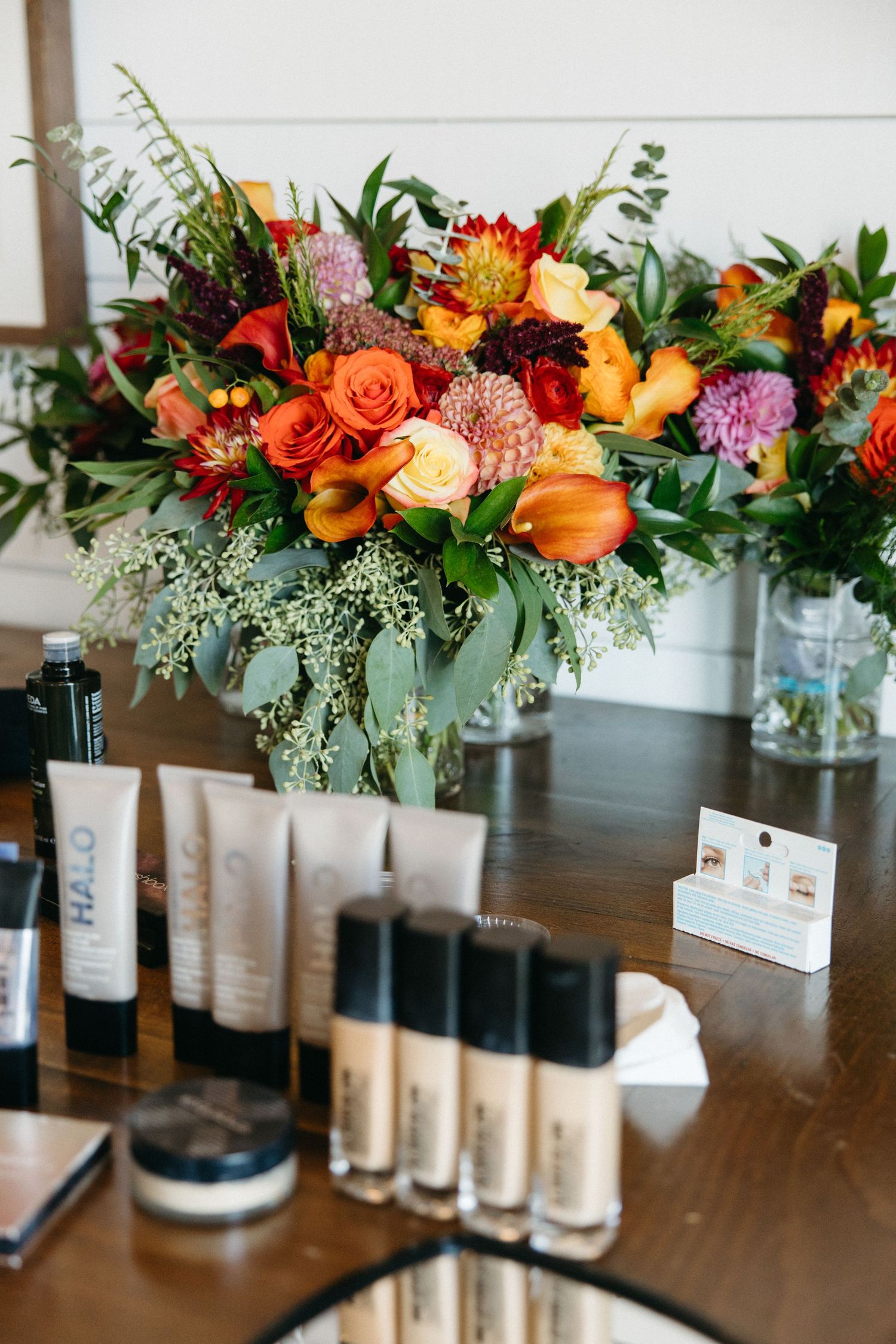 Vibrant floral arrangements with orange and pink flowers displayed alongside wine bottles on wooden table.