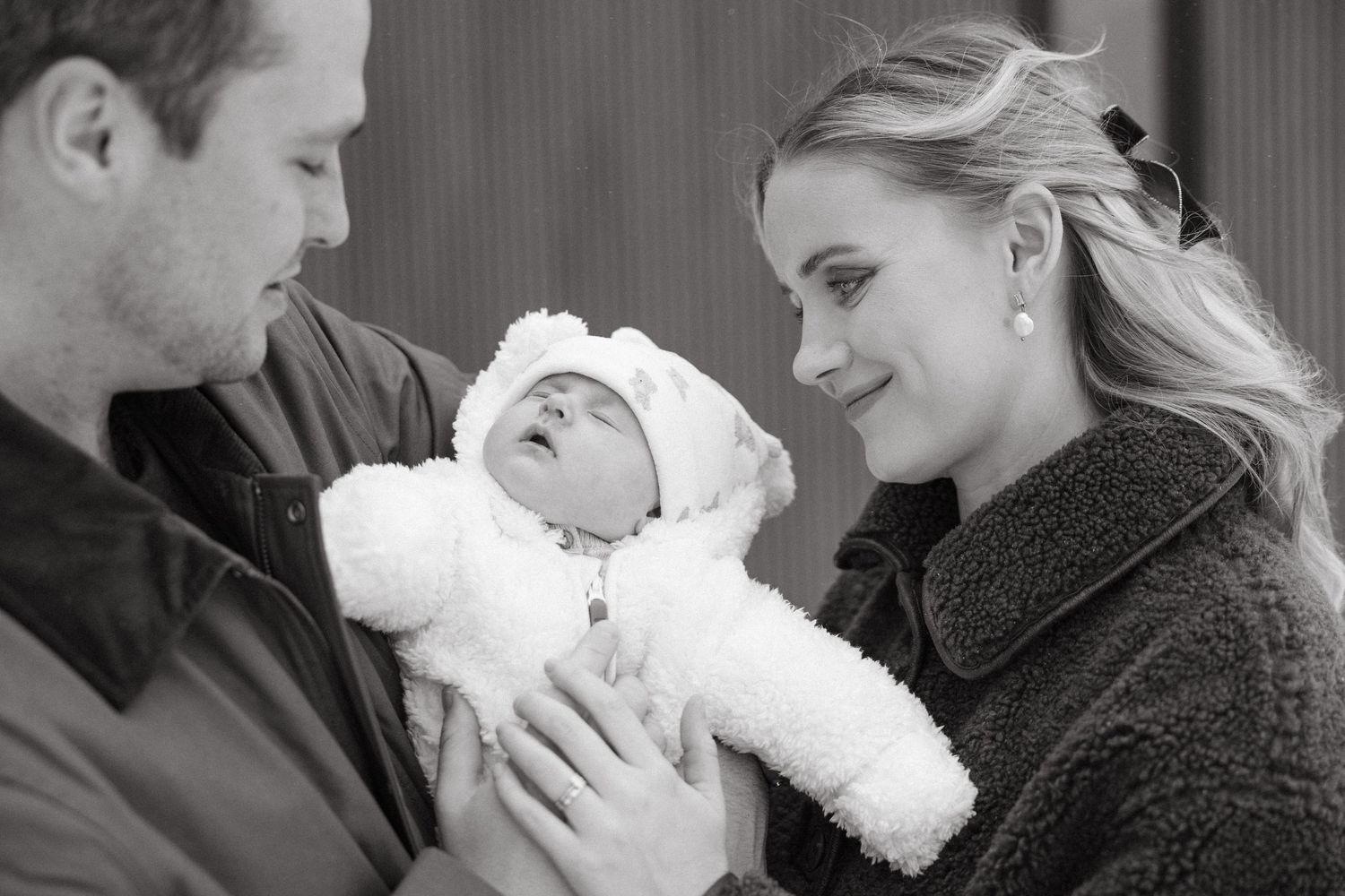 A couple gazes lovingly at their newborn baby bundled in a white outfit.