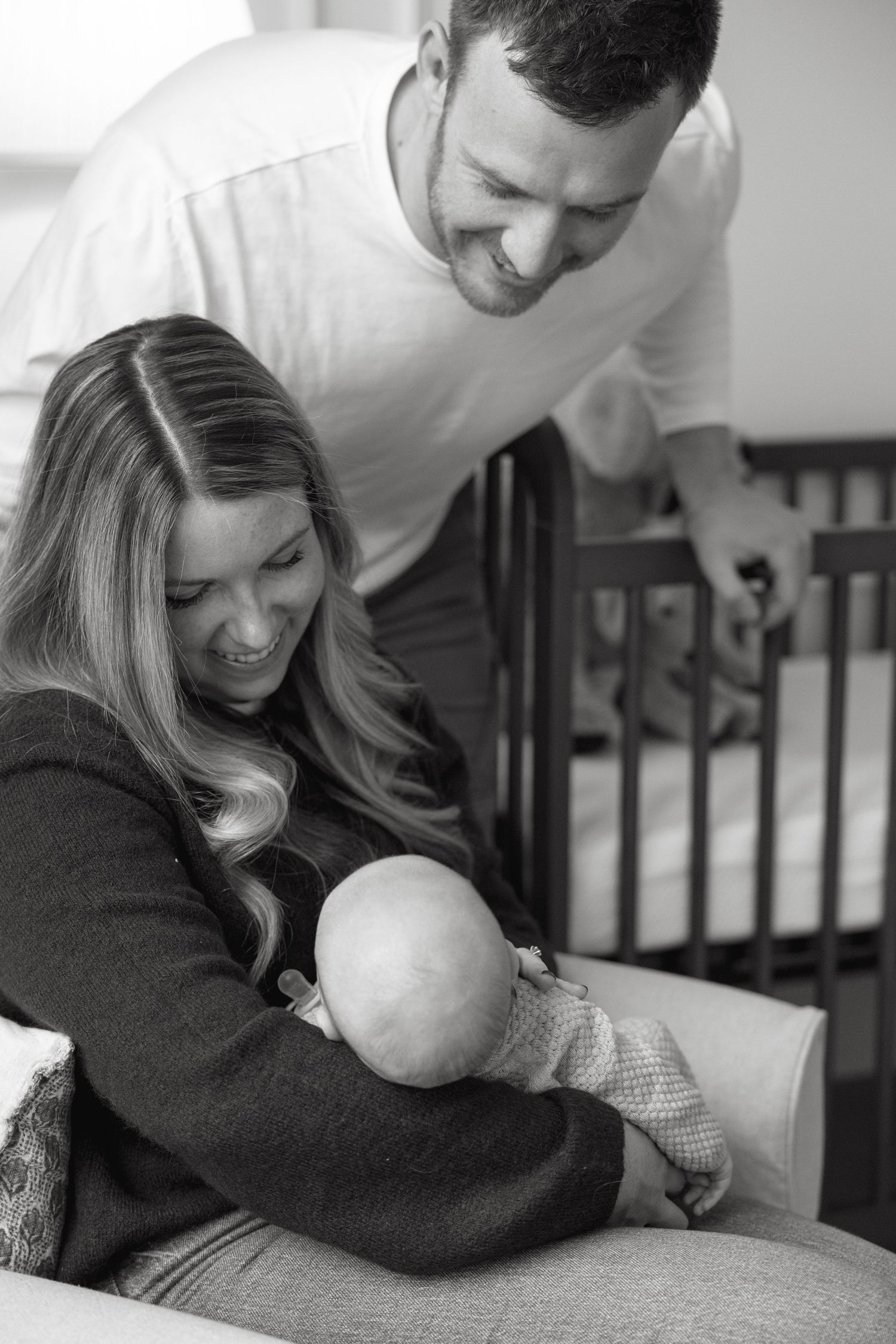 Black and white photo series of parents sharing intimate moments with baby near nursery crib.