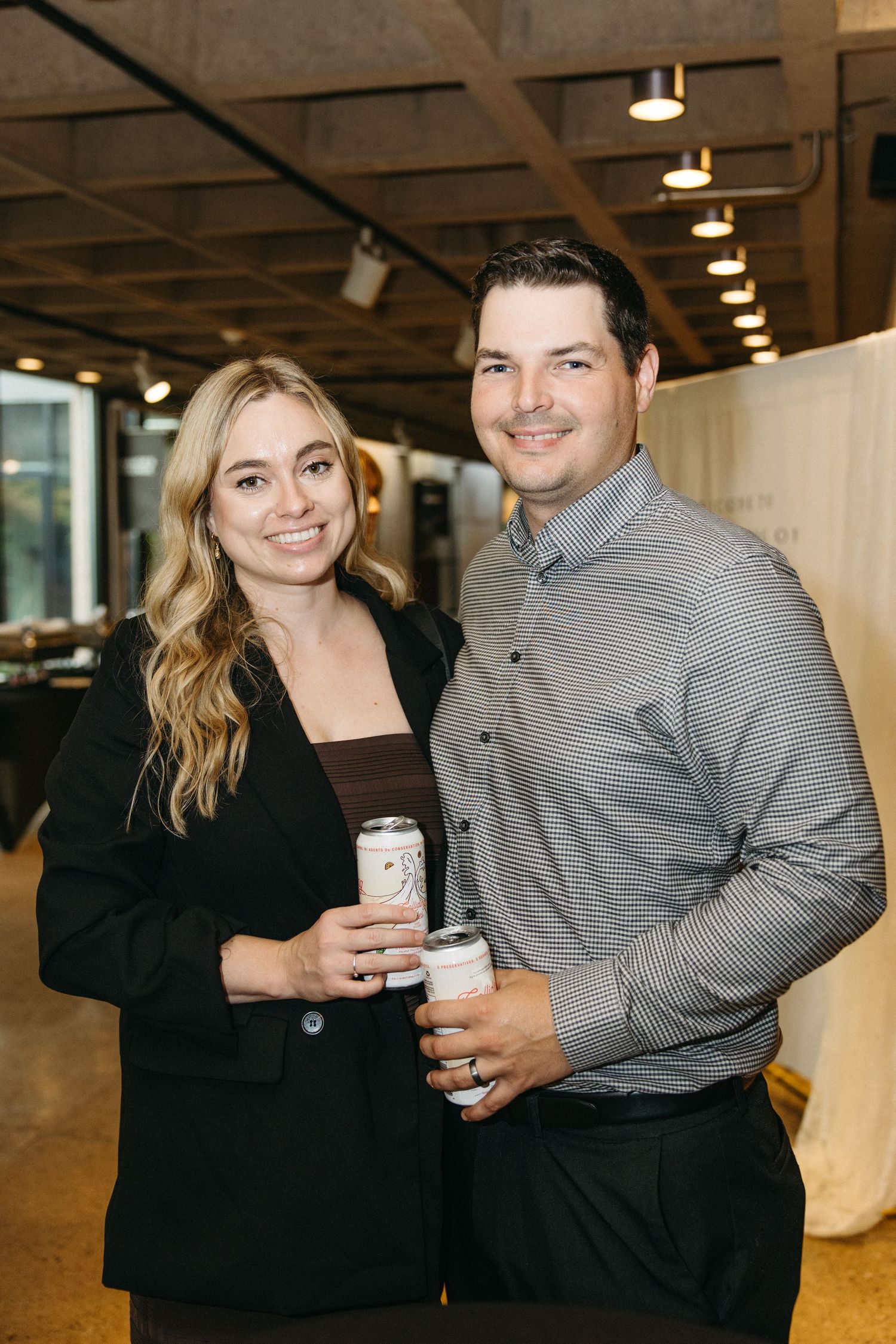 Couples in formal attire posing with drinks at an indoor event.