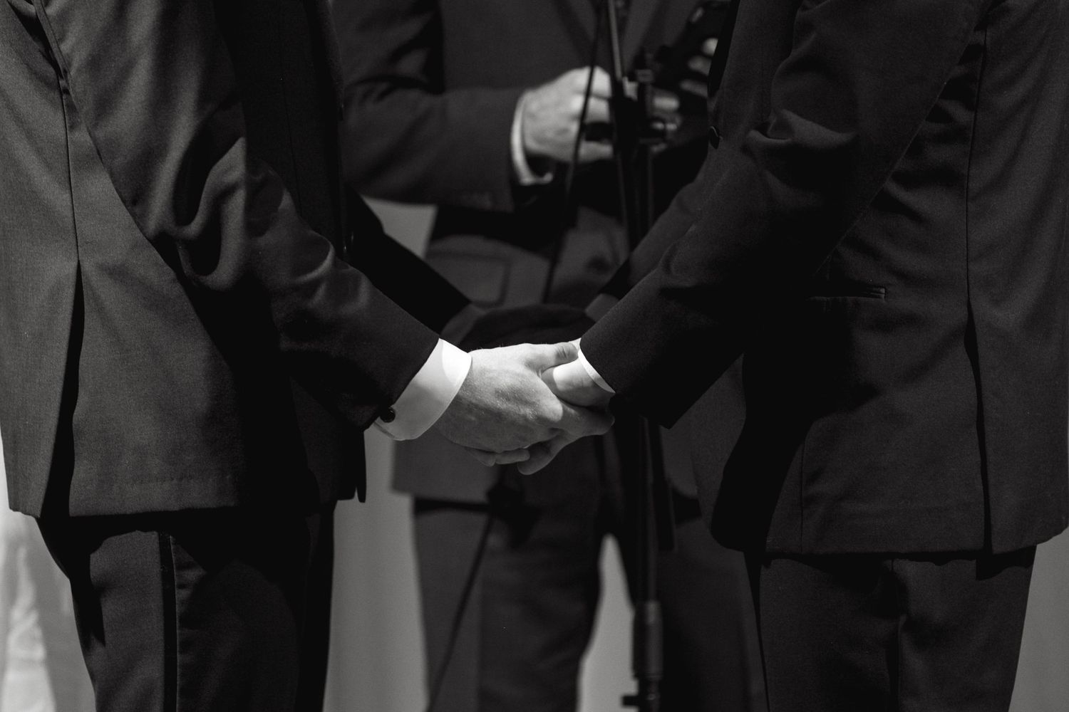 A black and white close-up of hands clasped together during a formal ceremony.