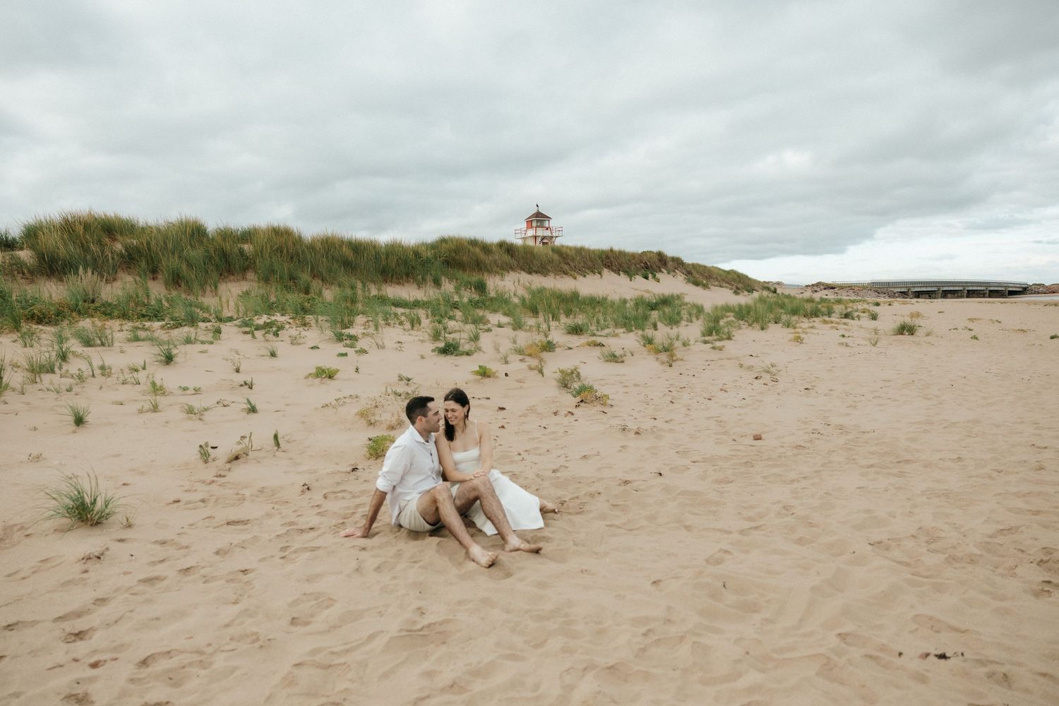 A couple enjoying a romantic moment on sandy beach dunes with coastal vegetation.
