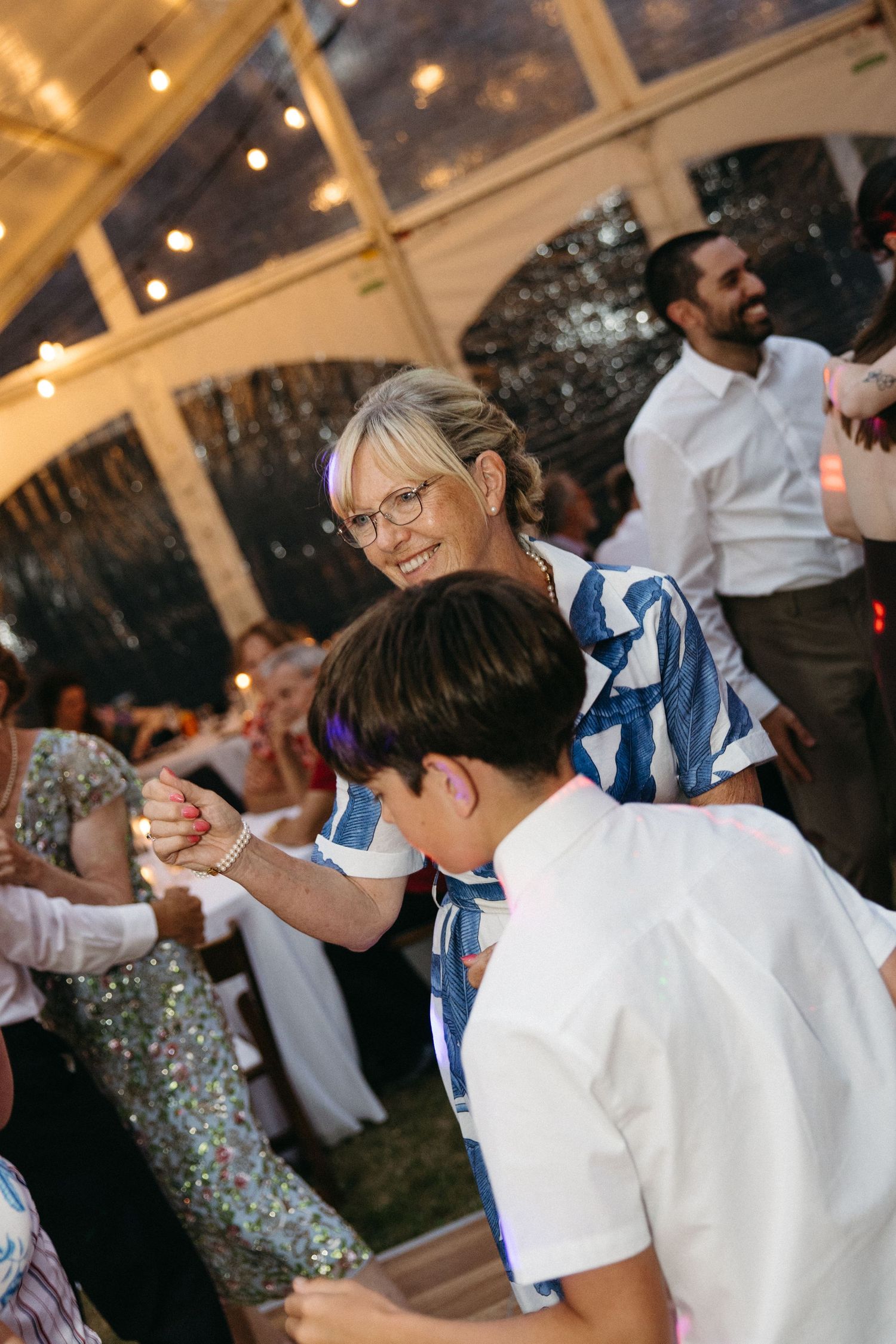 Guests dancing joyfully at elegant outdoor wedding reception under twinkling string lights.