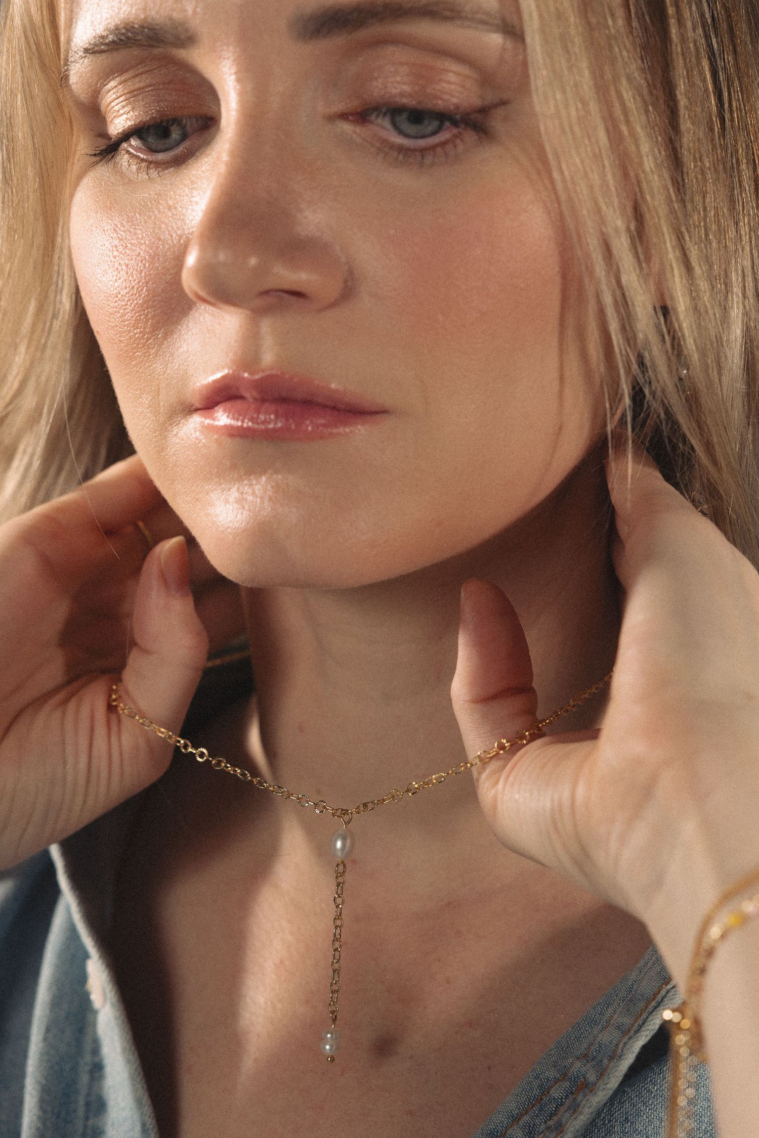 Dainty gold chain necklace displayed on model wearing denim against neutral background.