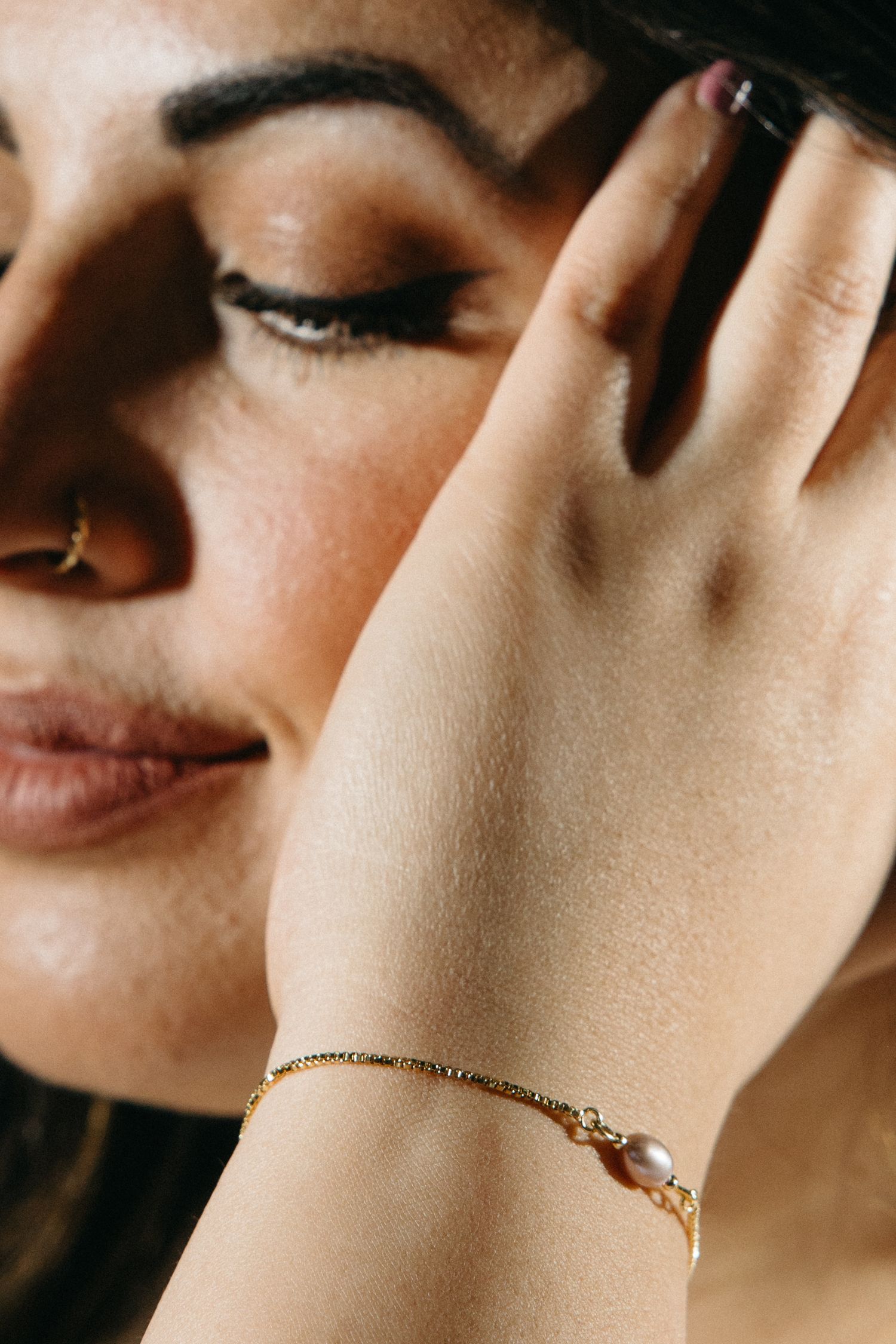 Close-up view of a delicate gold chain bracelet on a woman's wrist against a soft, blurred background.