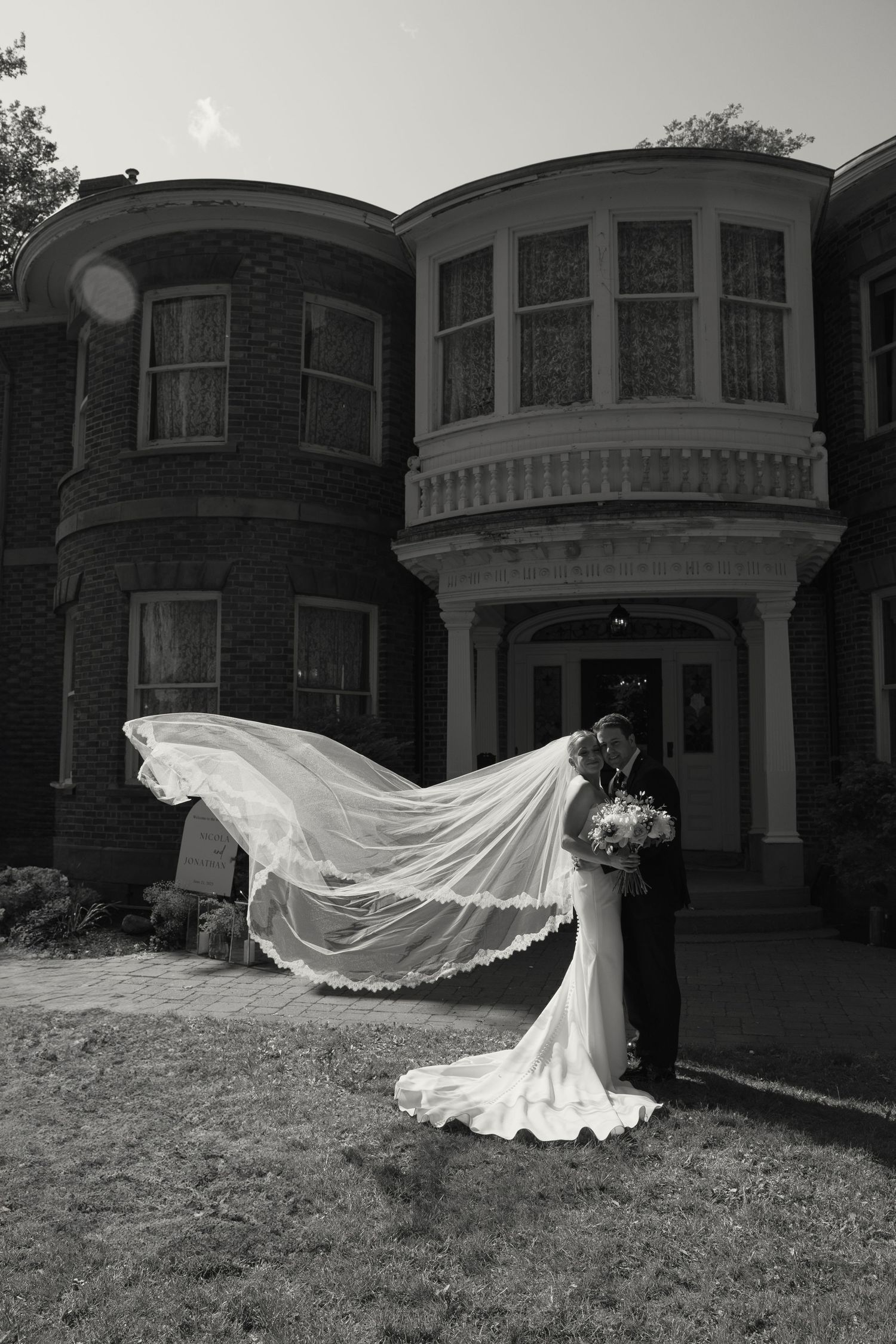 Dramatic black and white photo of a wedding veil flowing in the wind against historic mansion backdrop.