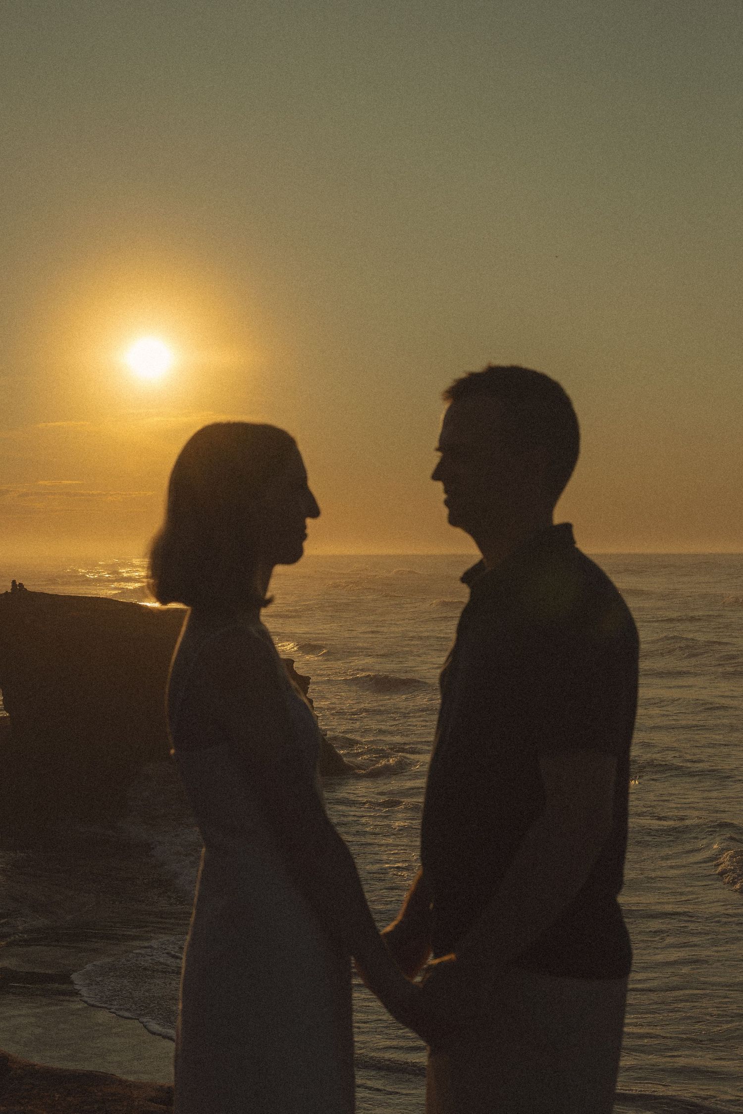 Silhouettes of two people against golden sunset over ocean waves.