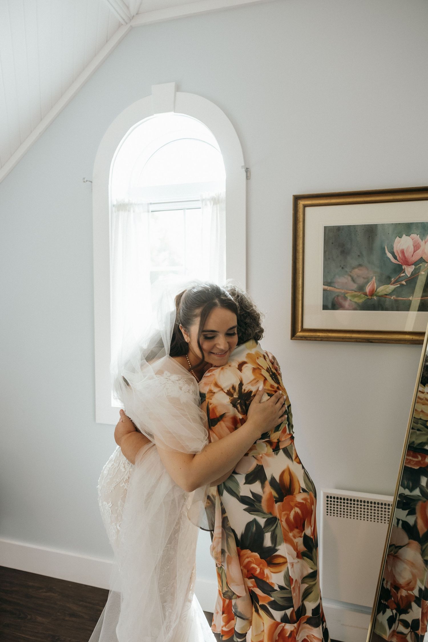 A tender embrace between loved ones in a bright sunlit room with floral artwork on the wall.