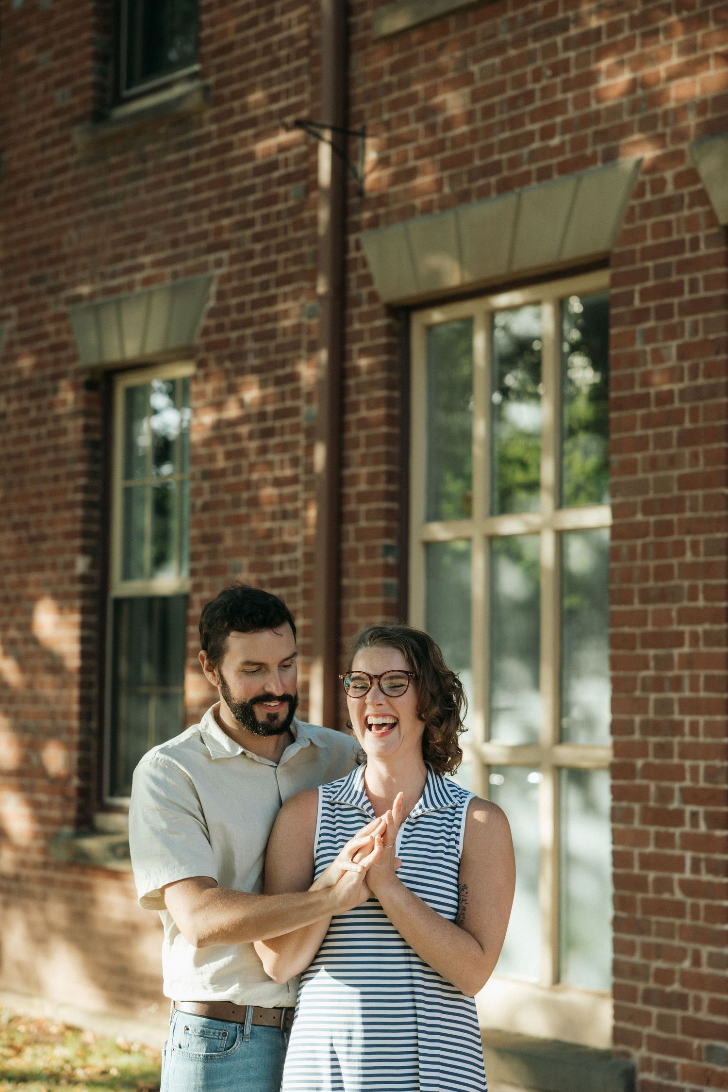 A joyful moment shared between two people outside a brick building in dappled sunlight.