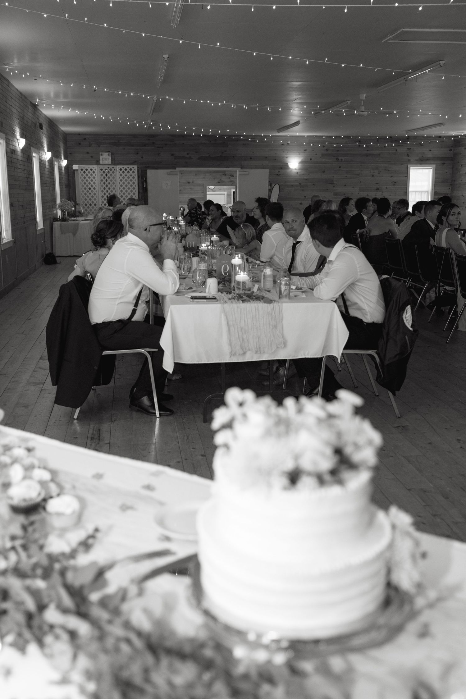 Wedding reception venue decorated with string lights and white tablecloths showing tables and a wedding cake.