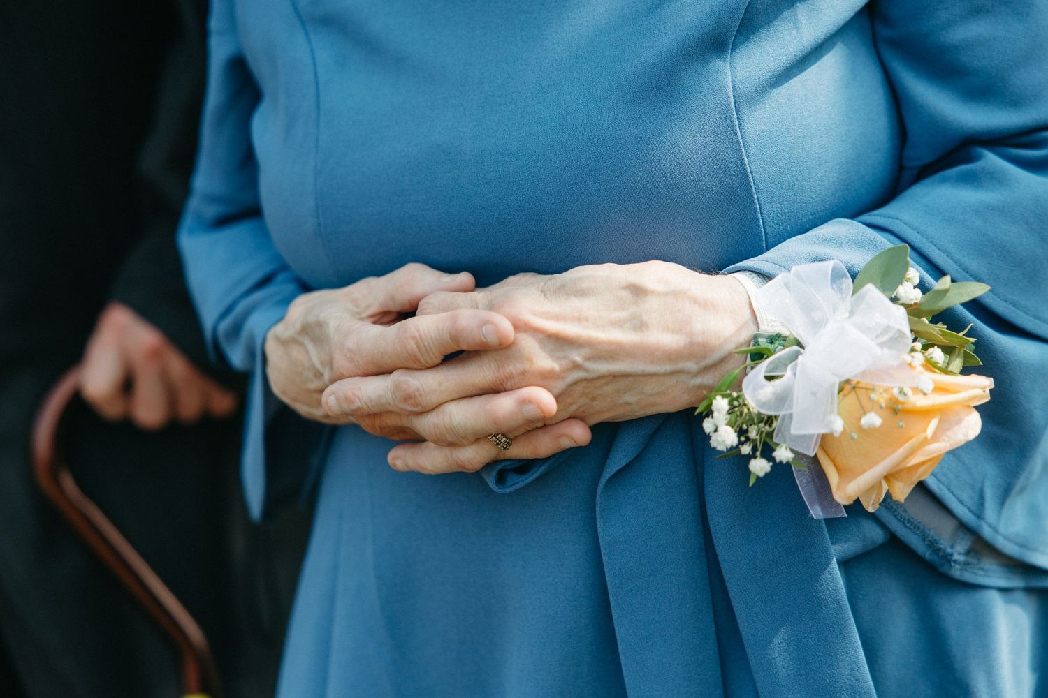Close-up of hands wearing blue attire holding delicate floral bouquet.