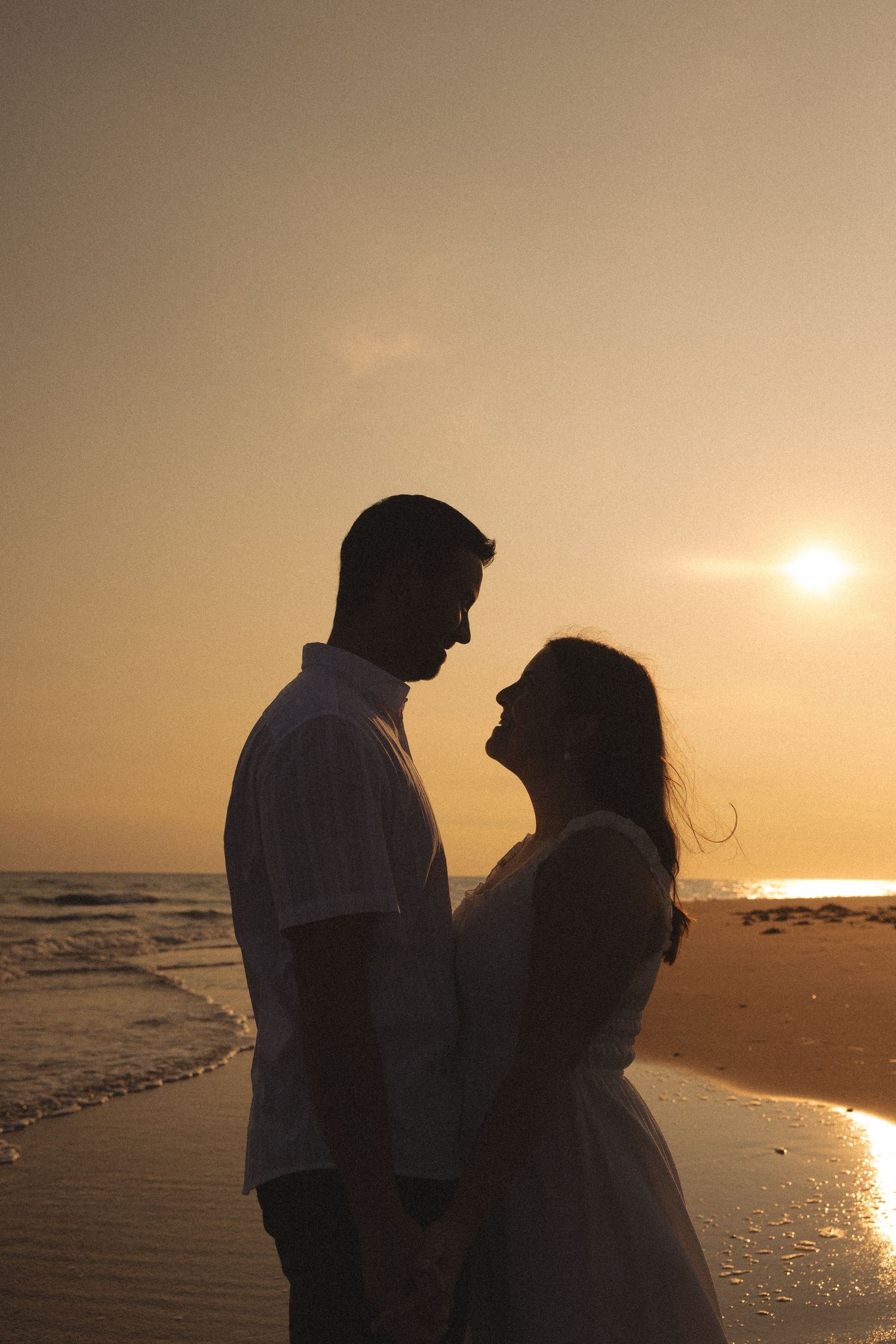 Silhouetted couple stands together on beach during golden sunset.