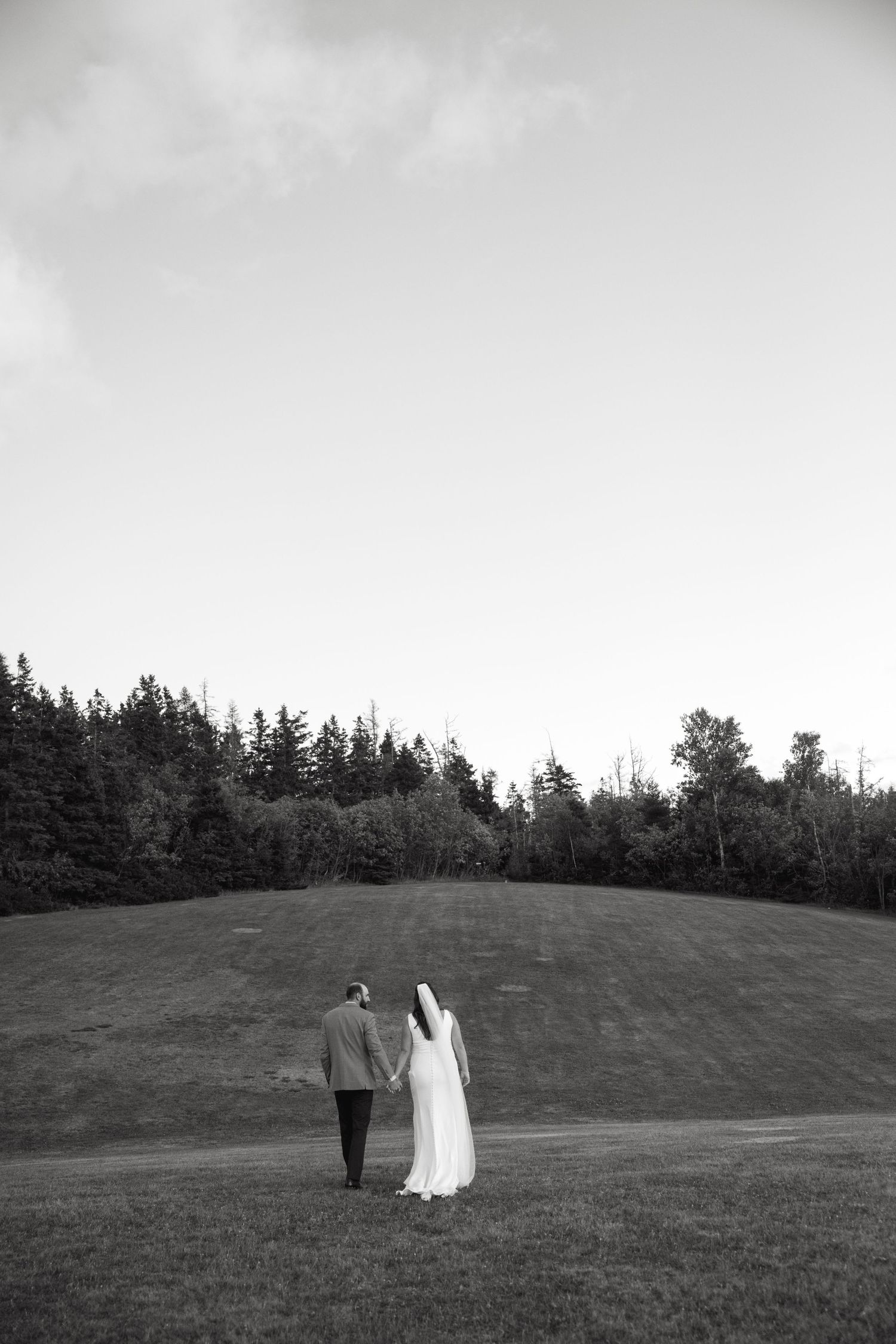 Black and white silhouettes of a couple walking on a grassy hillside with trees in background.
