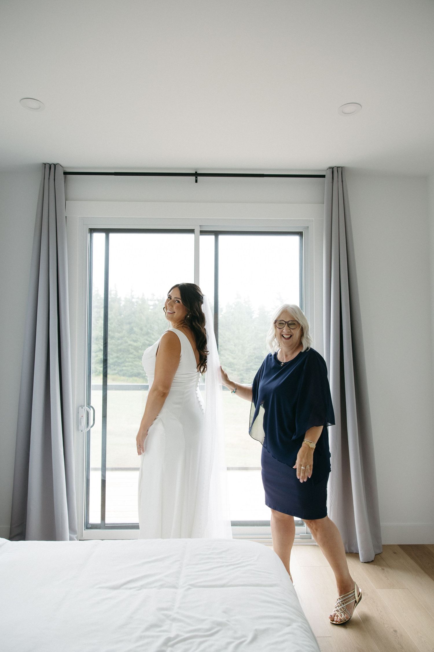 Bright modern bedroom interior with white bedding and floor-length grey curtains.