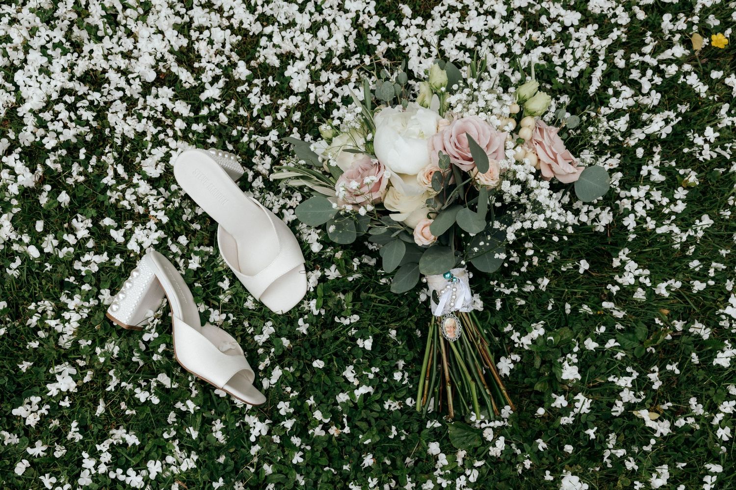 Wedding accessories including shoes and bouquet arranged on flower-covered ground.