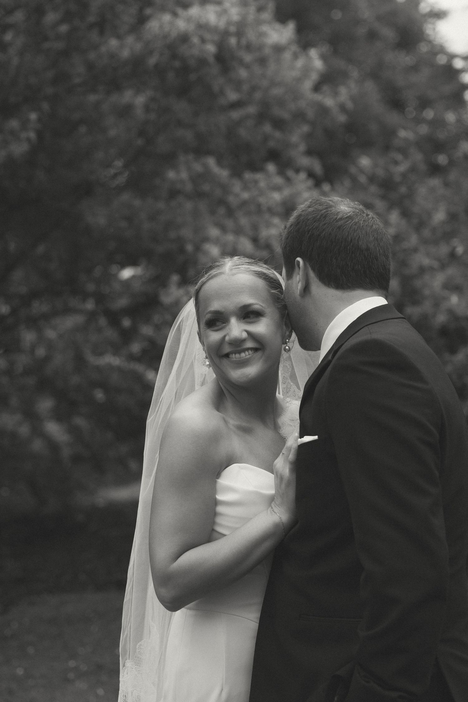 Candid black and white wedding moment captured in a garden setting.