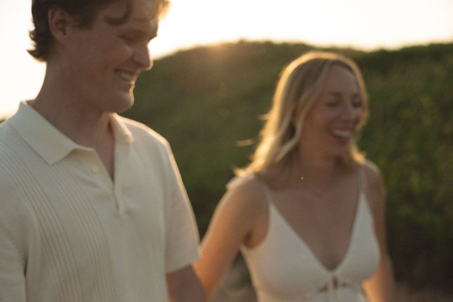 A smiling couple walks outdoors at golden hour, with lush greenery in the warm sunset background.