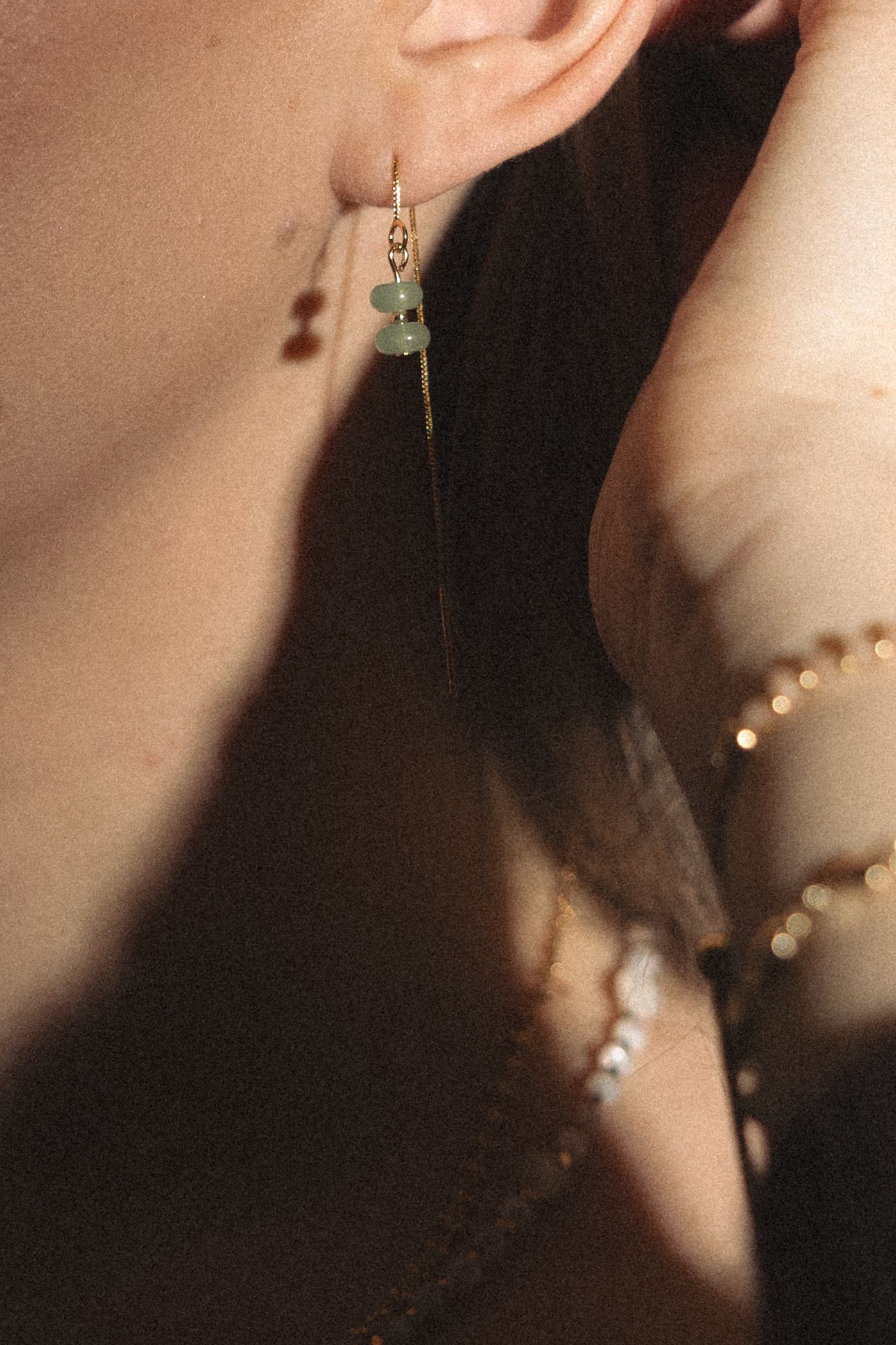 A series of blurred close-up photos showing a delicate silver earring with a green gemstone against a soft background.
