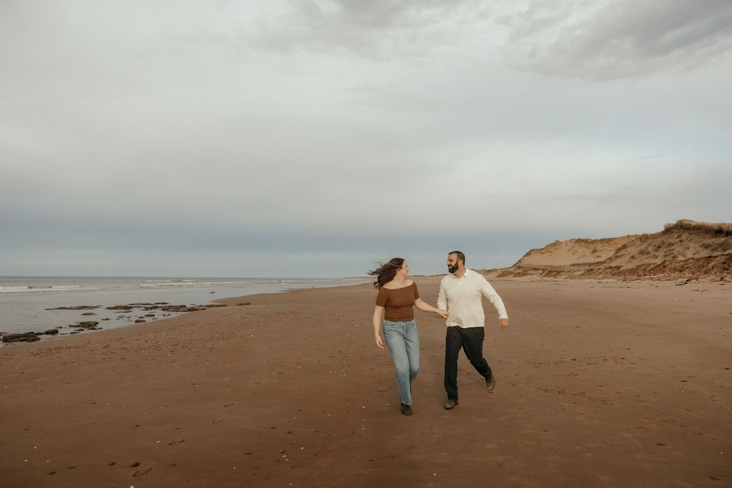 Romantic couple walking and embracing along a cloudy beach shoreline.