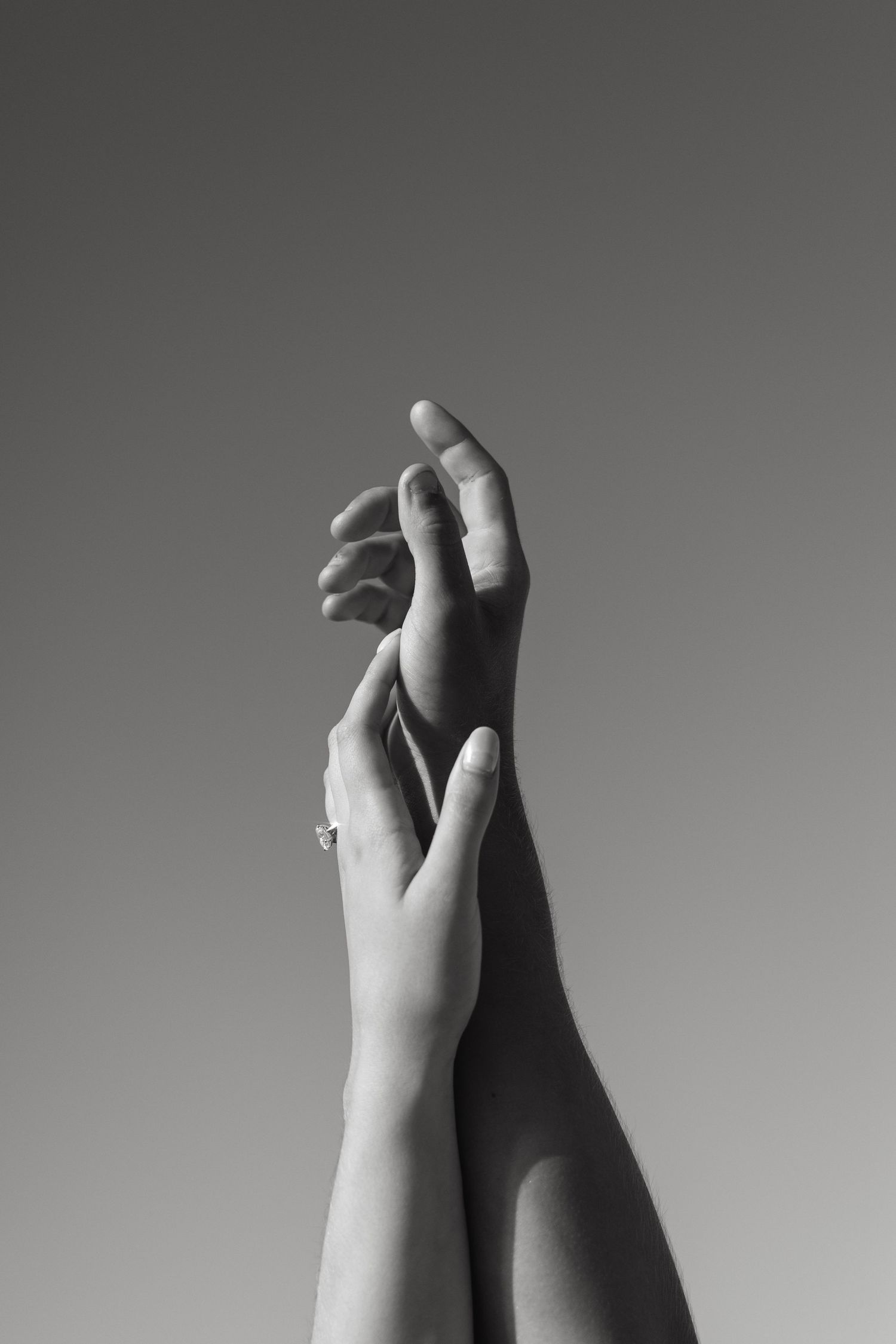 Black and white photo of two hands reaching upward, one adorned with a diamond engagement ring.