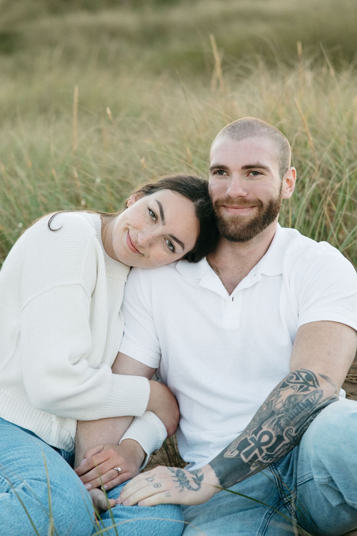 Couple relaxing together in tall grass wearing white and denim.