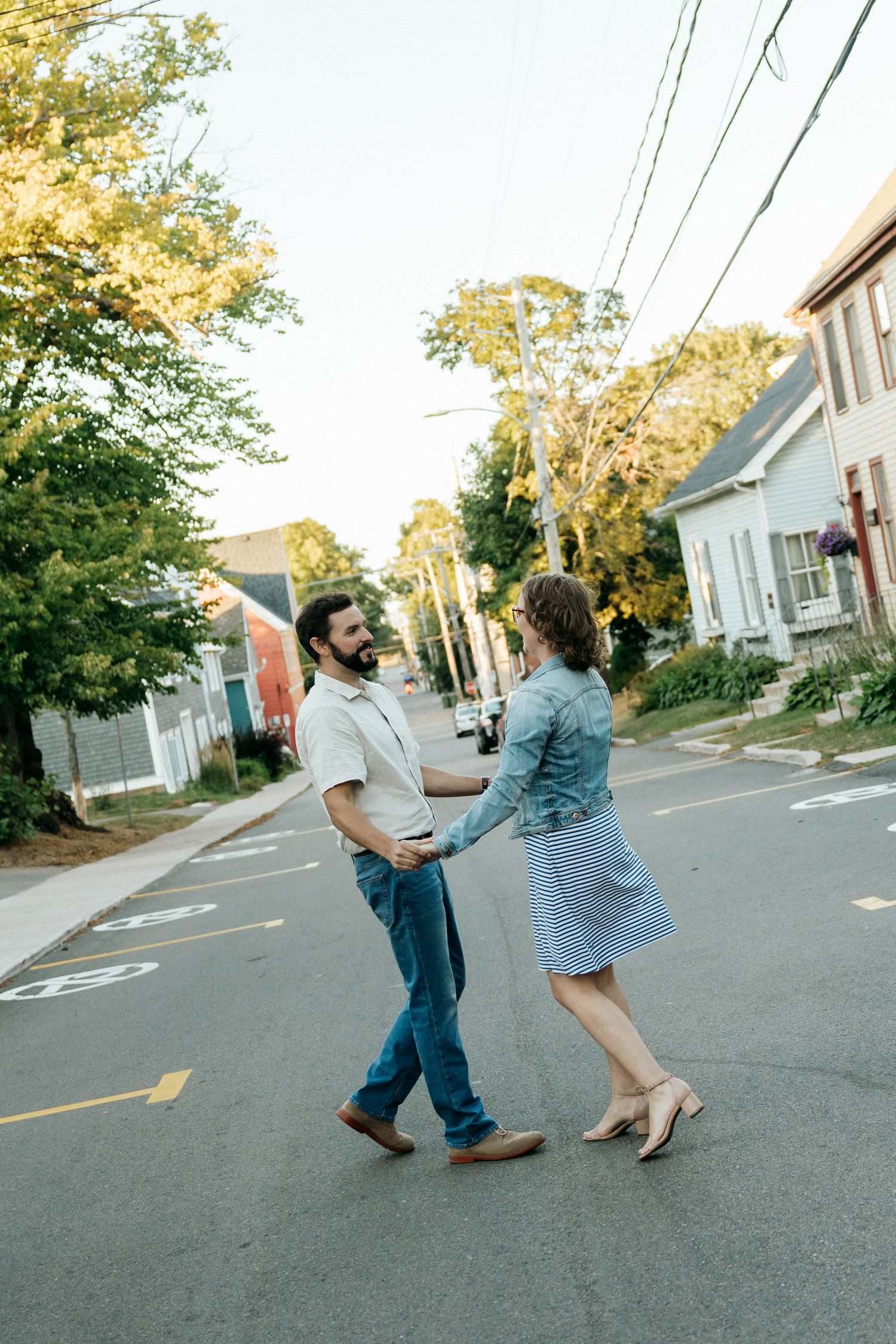 A playful couple dances together on a residential street lined with colorful houses.