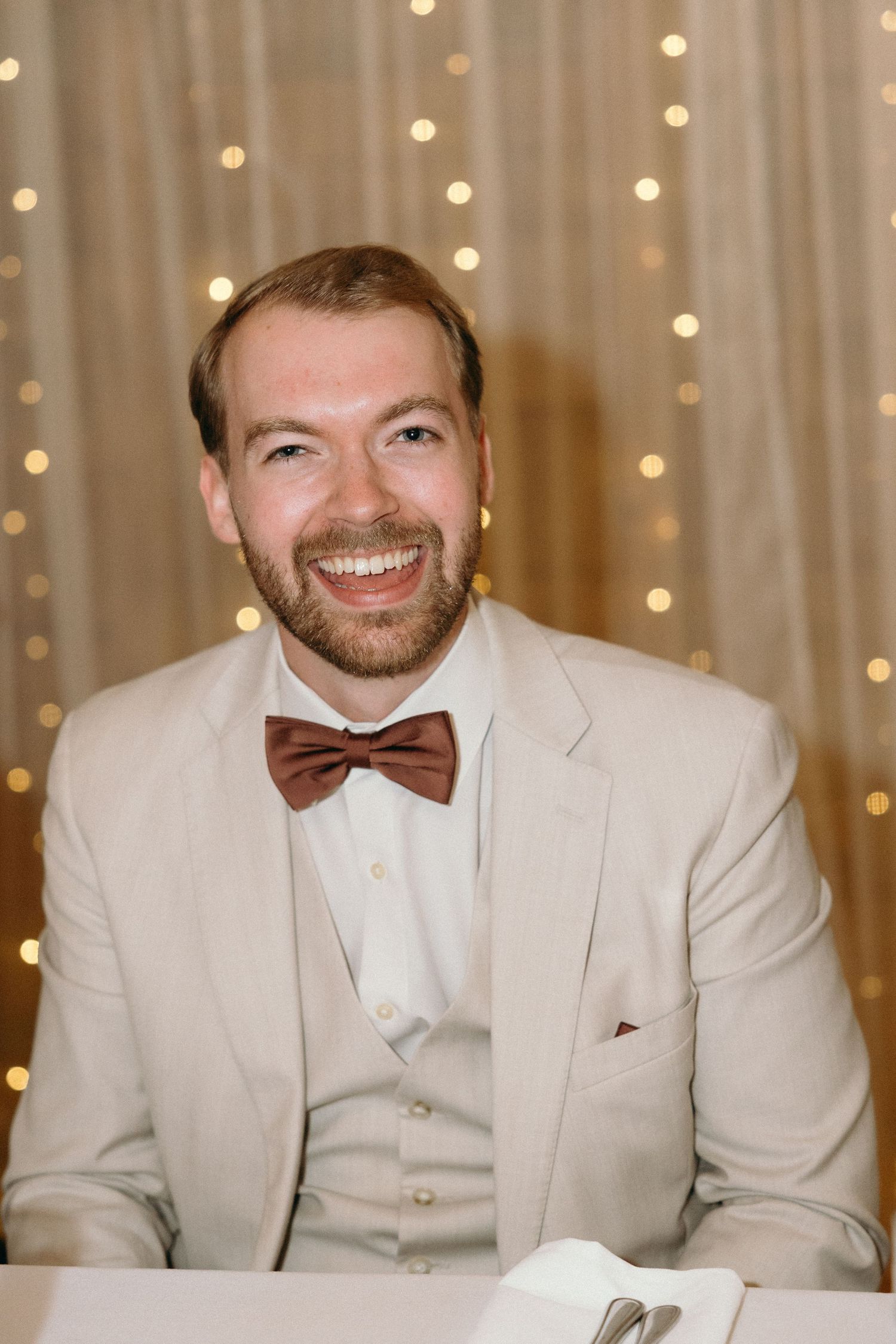 Wedding party members in cream colored suits and bow ties against twinkle light backdrop.
