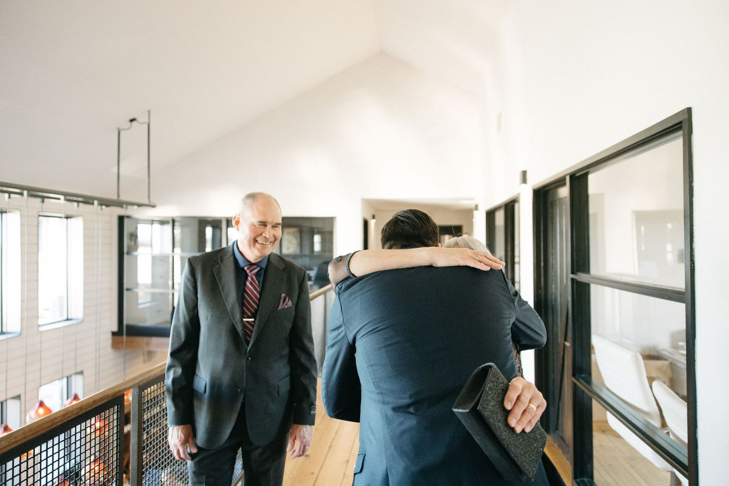 People walking through modern office hallway with glass walls and natural light.