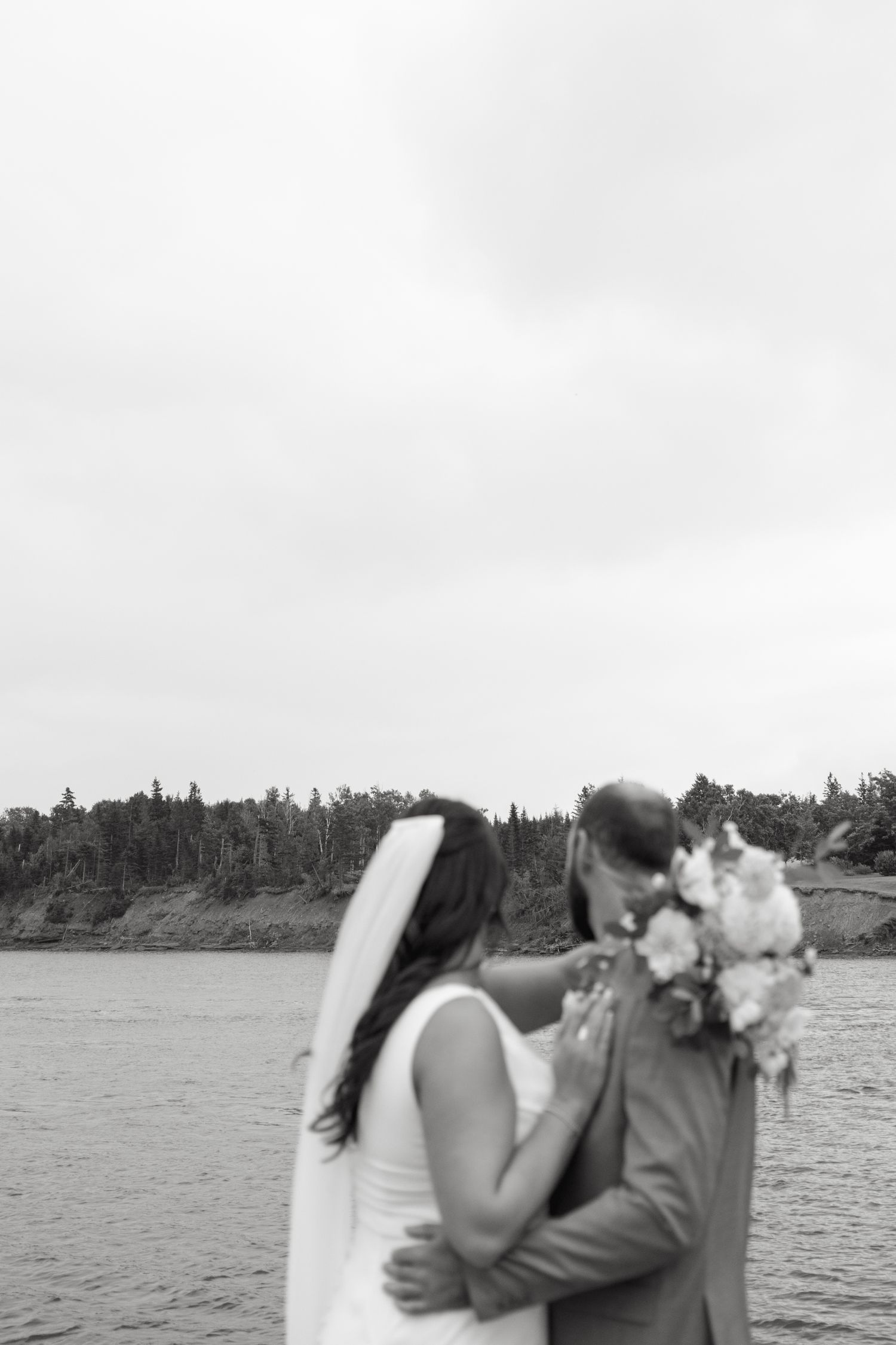 Intimate lakeside wedding portraits with flowing veil in black and white.