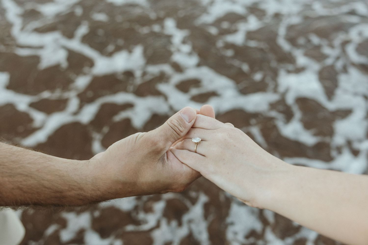 Close-up shot of two hands reaching toward each other against a blurred water background.
