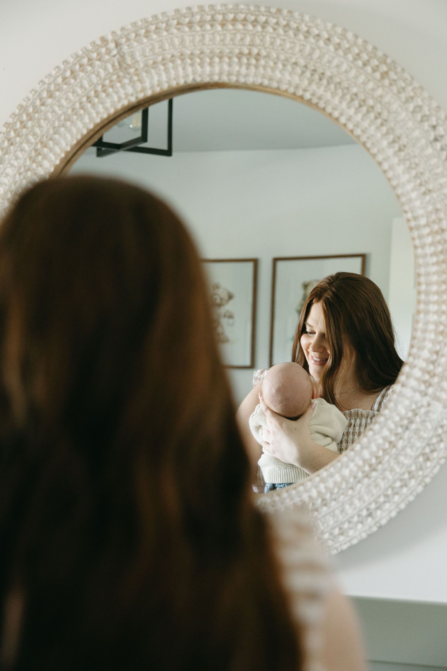 A decorative oval mirror with a textured white frame hangs on a light-colored wall.