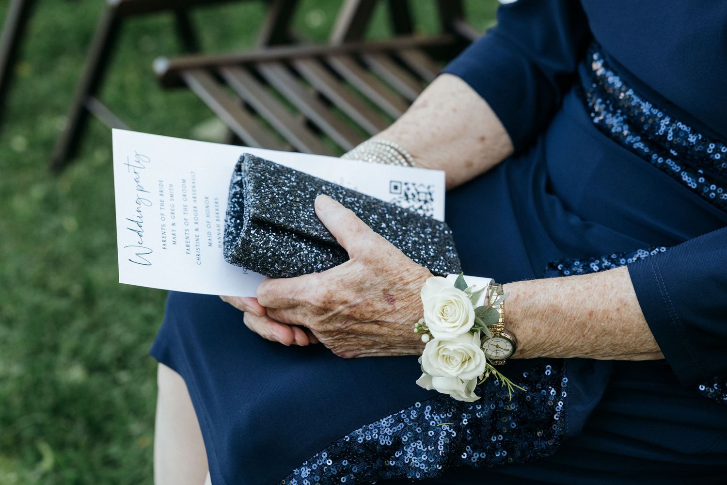 Hands holding a wedding program with white rose corsage detail.