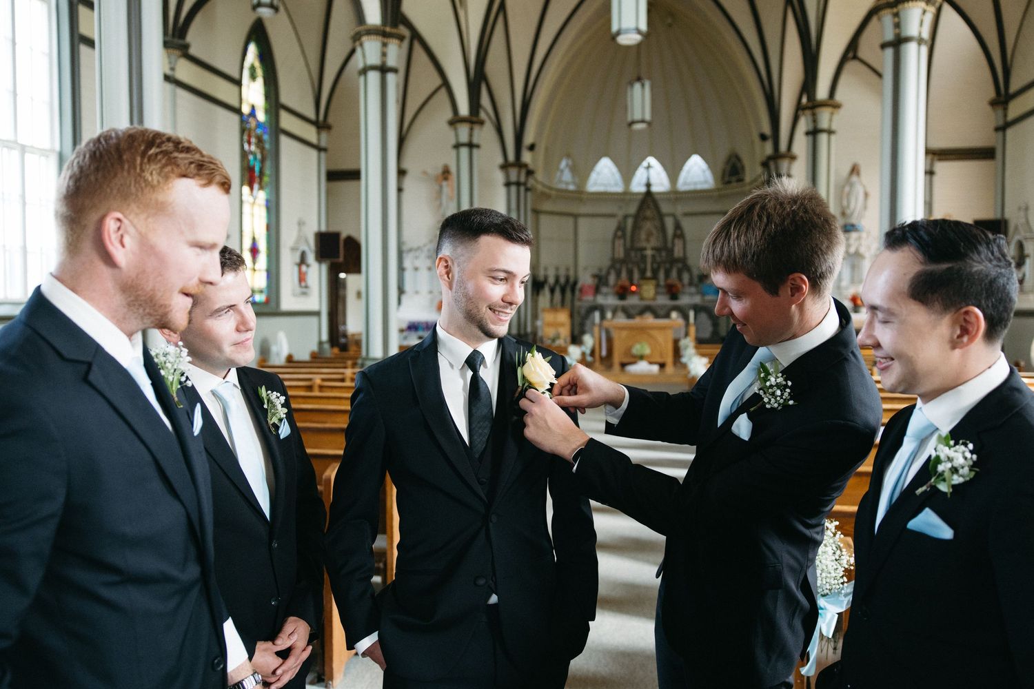 Groomsmen in black suits gather in a church with gothic architecture.