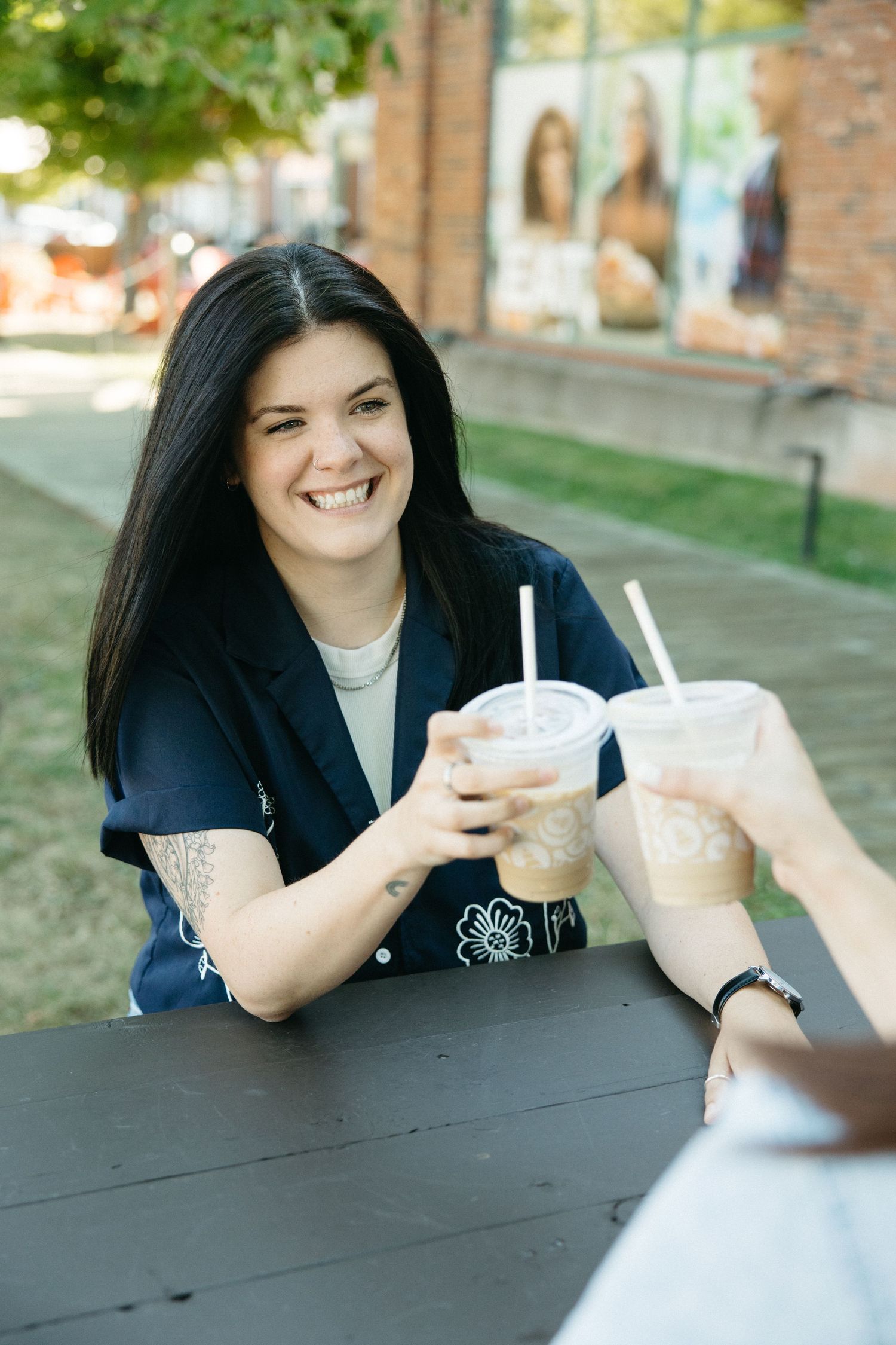 Two people sharing drinks and conversation at an outdoor table on a sunny day.