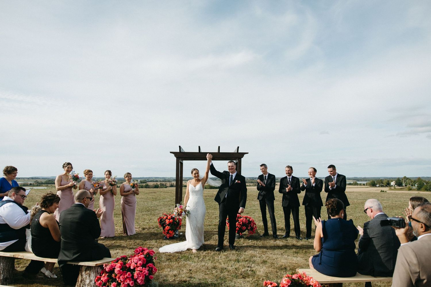 Wedding ceremony setup with rows of chairs facing a wooden arch against a cloudy sky.
