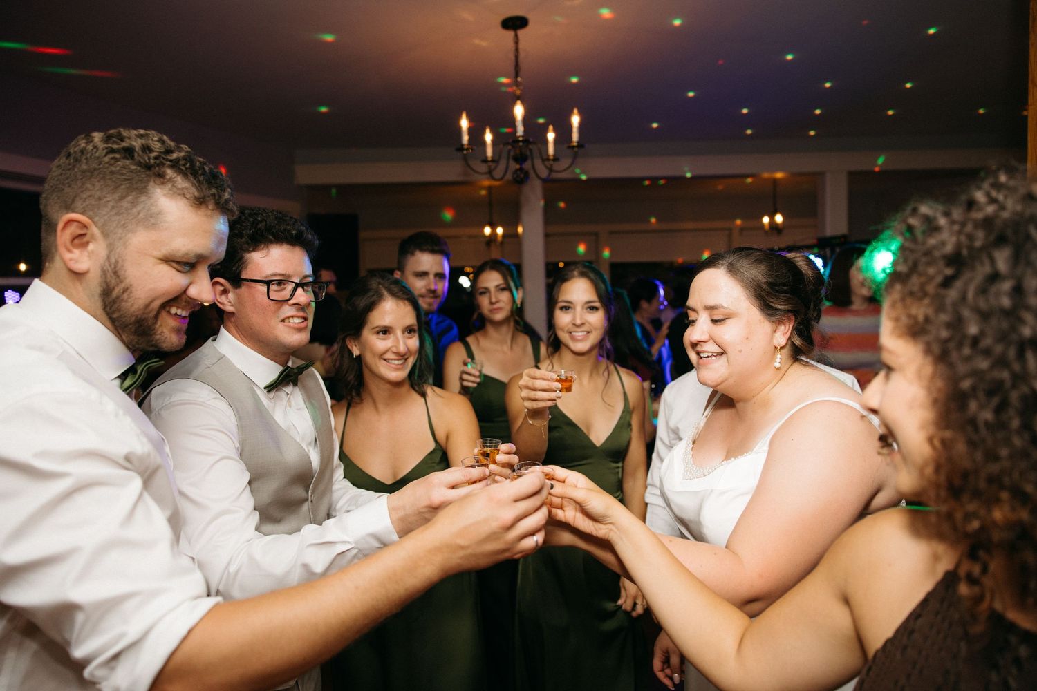 Wedding party clinking shot glasses together in a celebratory toast on the dance floor.