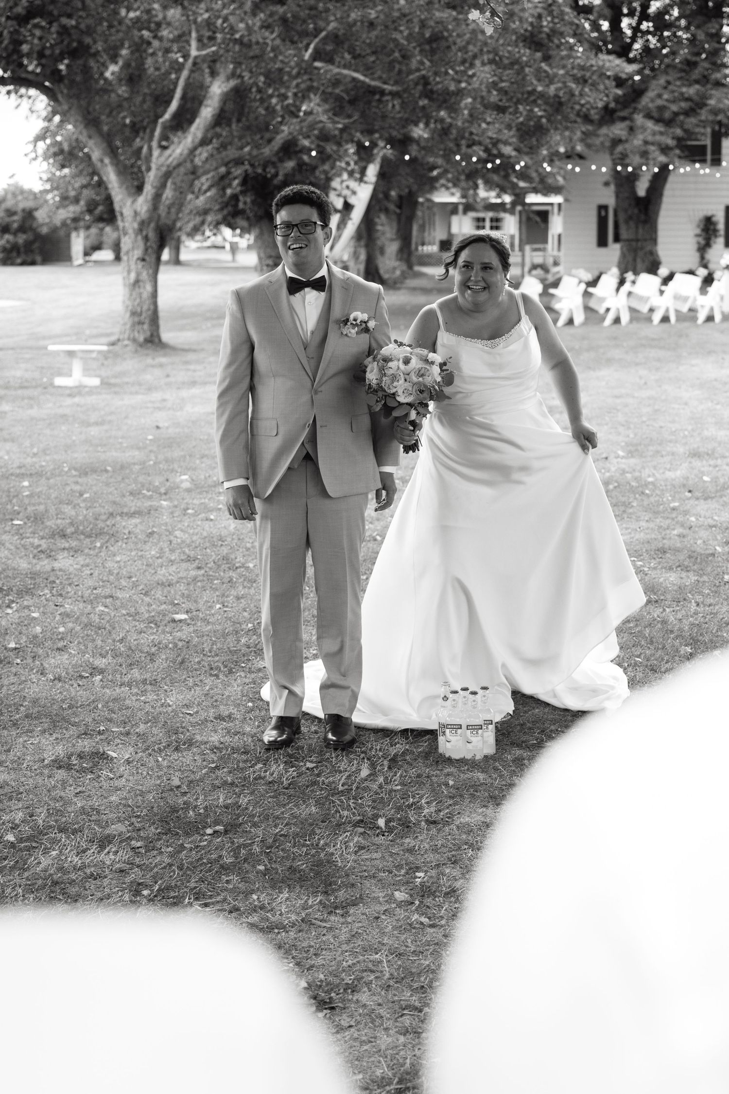 Black and white photo of smiling bride and groom walking down the aisle together at an outdoor wedding ceremony.