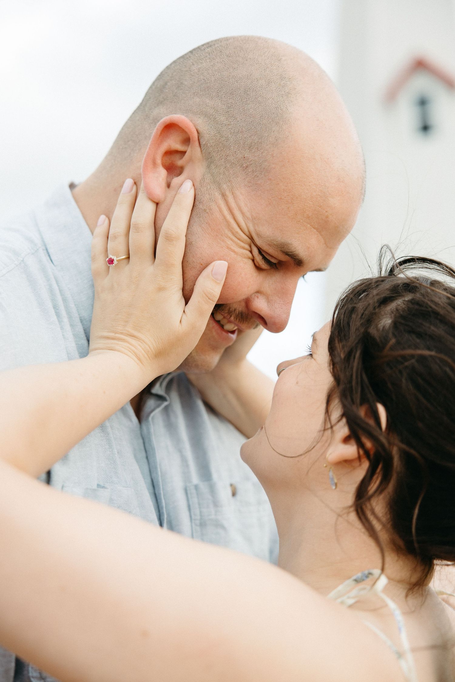 Couple sharing a tender moment, woman gently cupping bald mans face as they smile nose to nose.