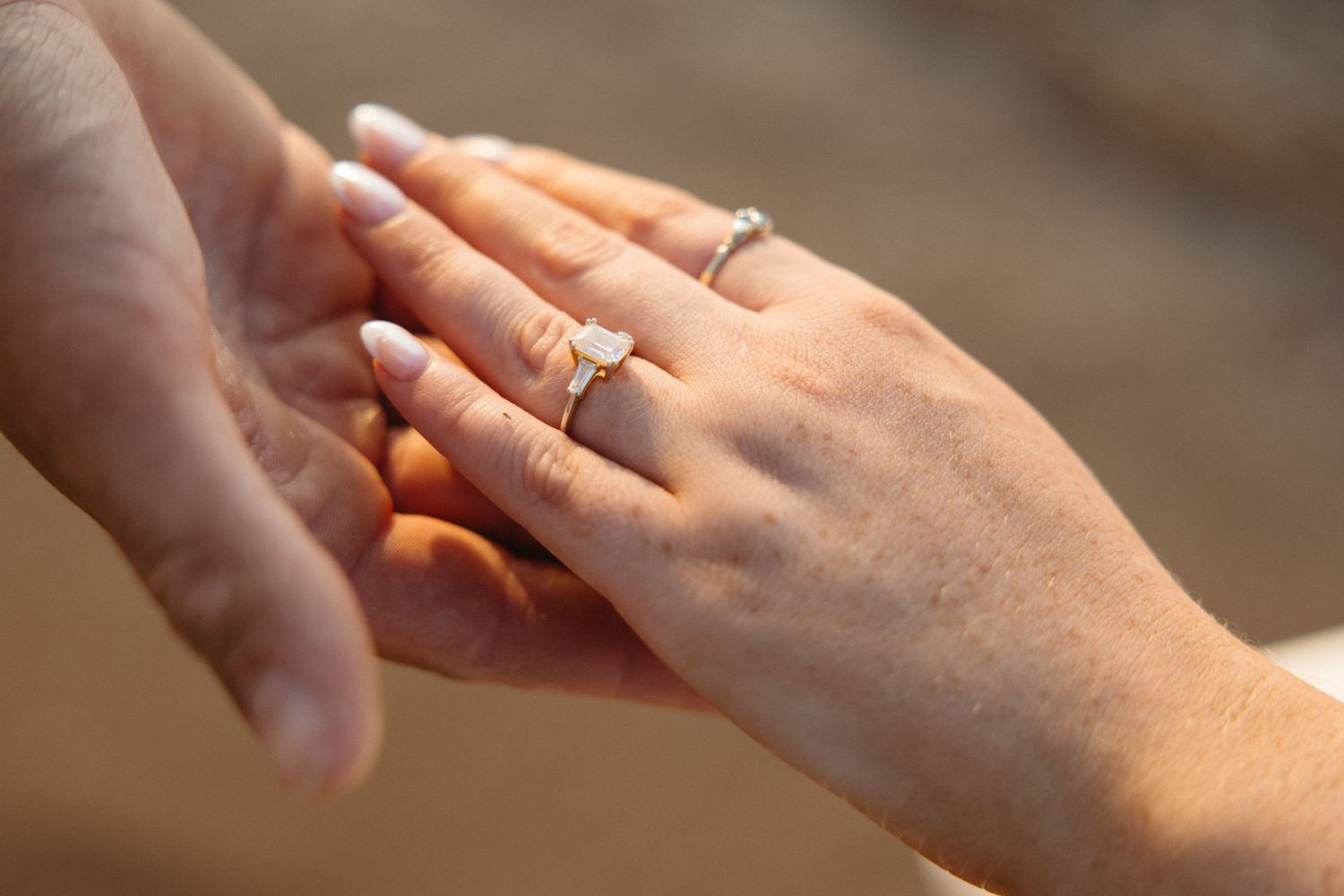 Close-up of two hands with elegant diamond engagement rings, symbolizing love and commitment.