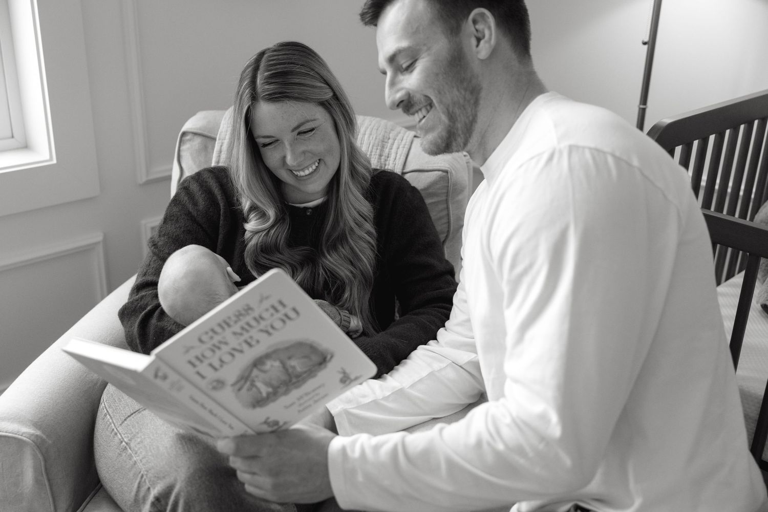 A couple smiles while reading a book together in their living room.