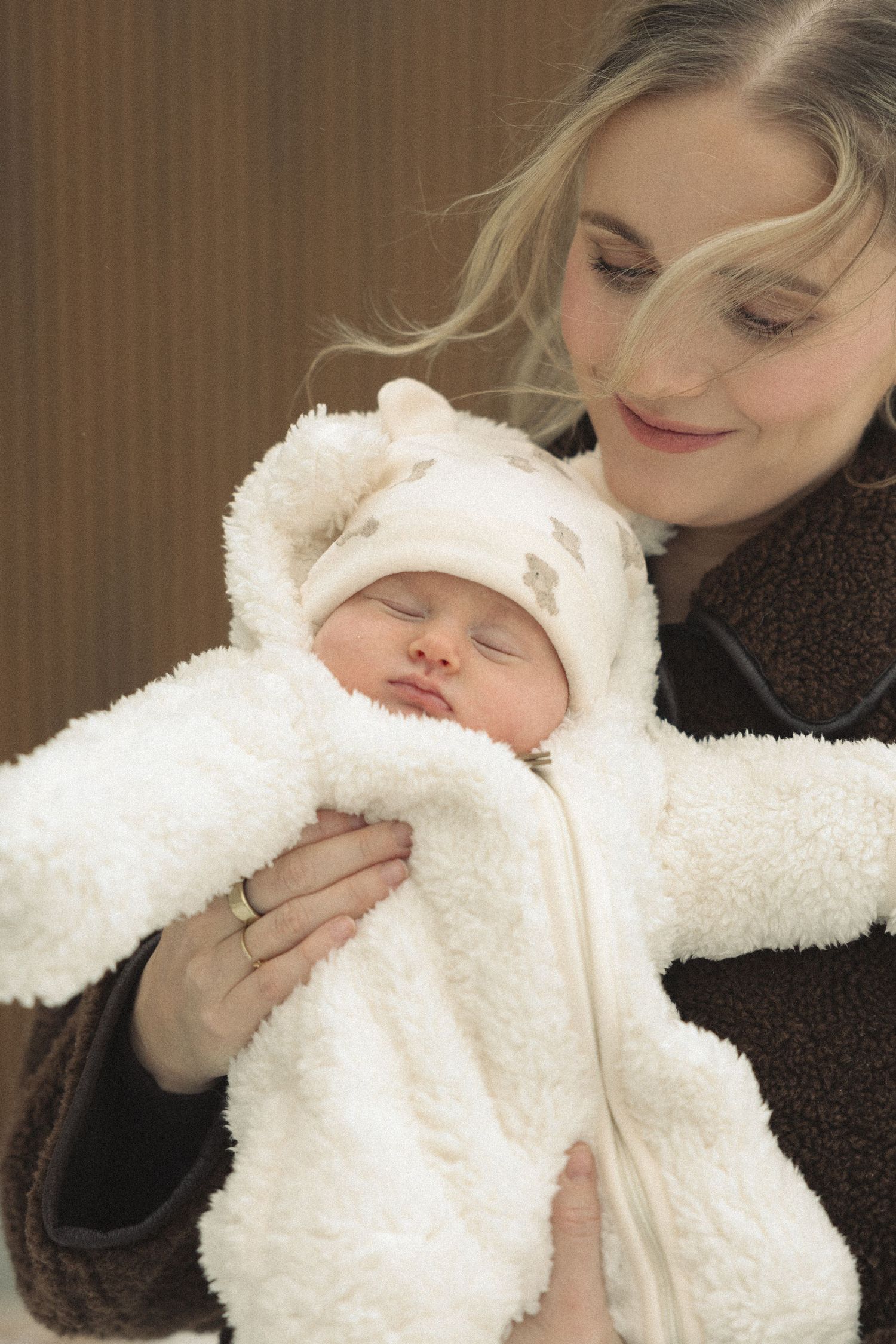A sleeping newborn wearing a cozy white winter outfit is held tenderly.