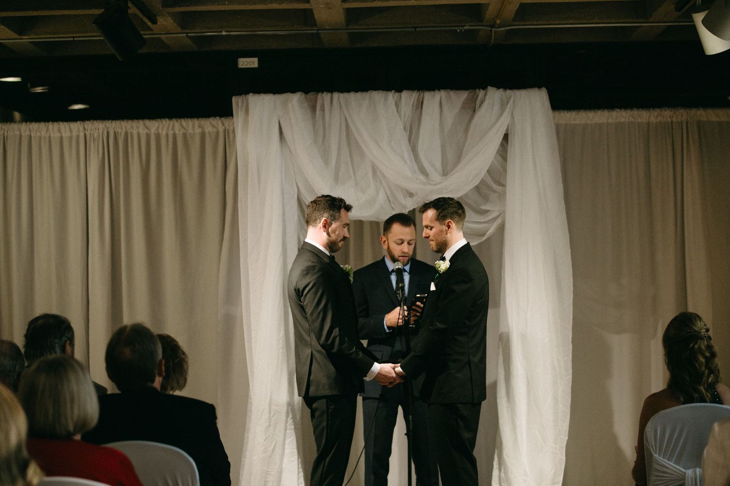People gathered in formal attire at an indoor event with white curtains in the background.