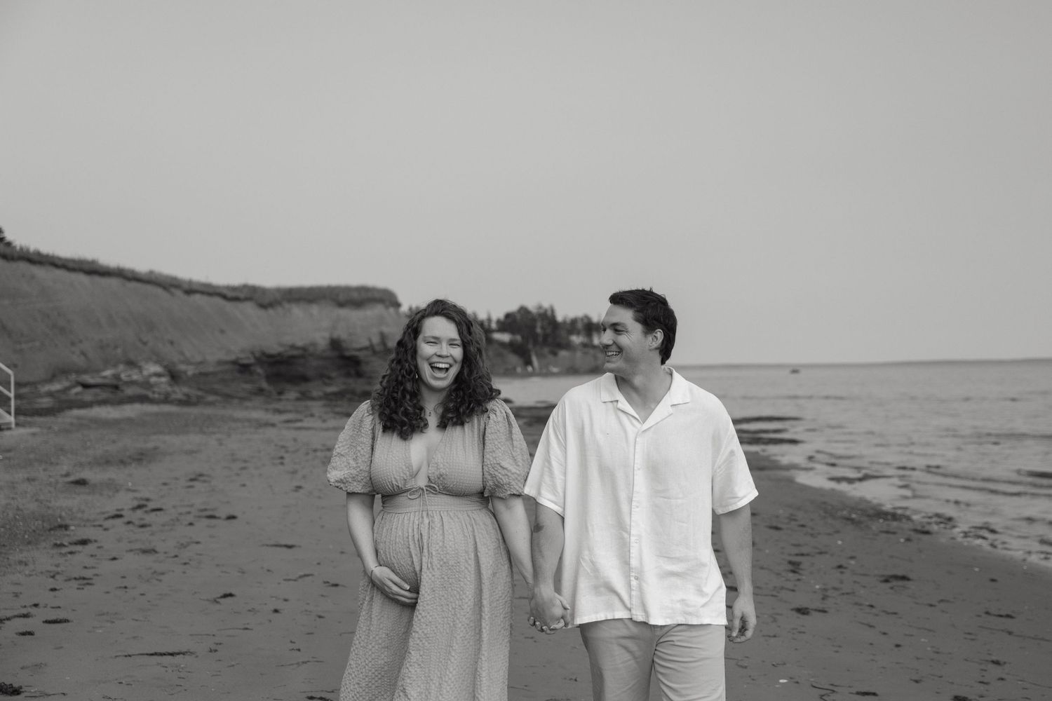 Black and white photo of a couple walking along a coastal beach landscape.