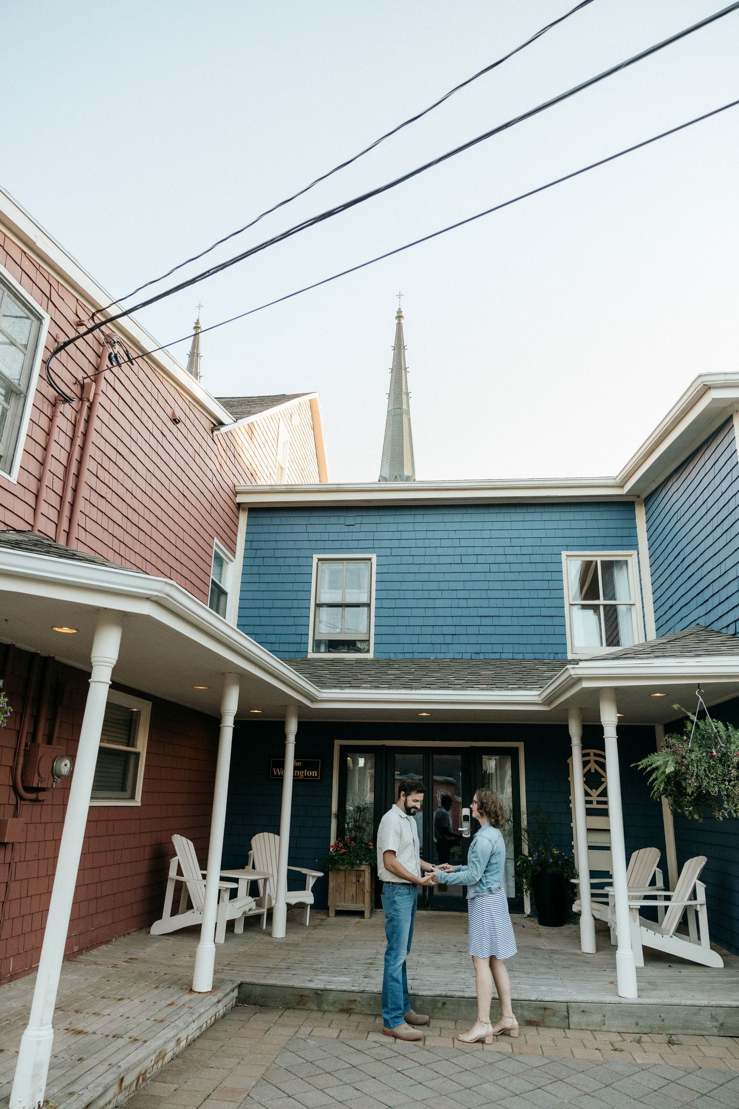 A couple stands beneath white columns outside a blue and red building.