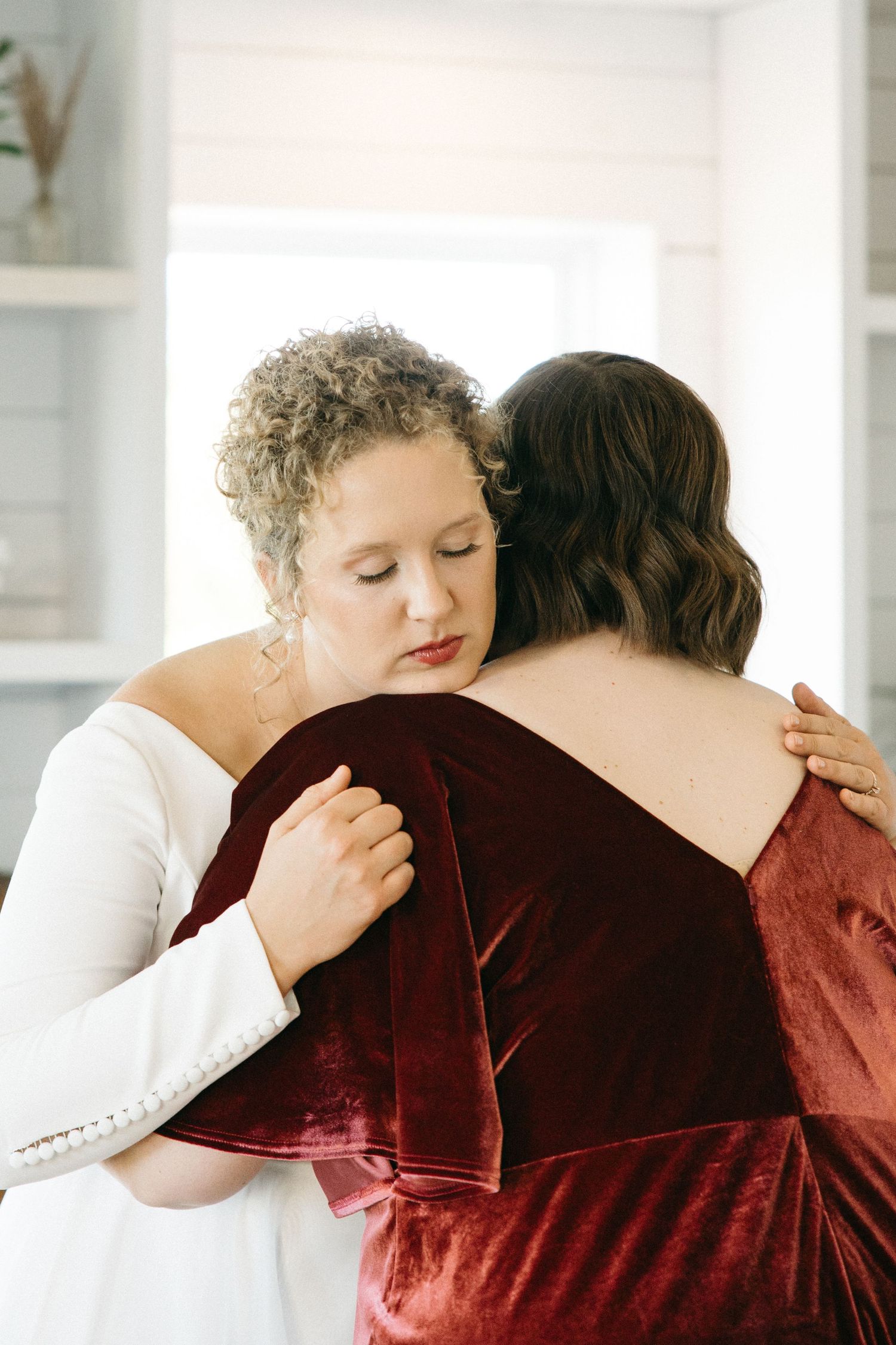 Two people share an intimate embrace, one wearing white and one in deep red velvet.