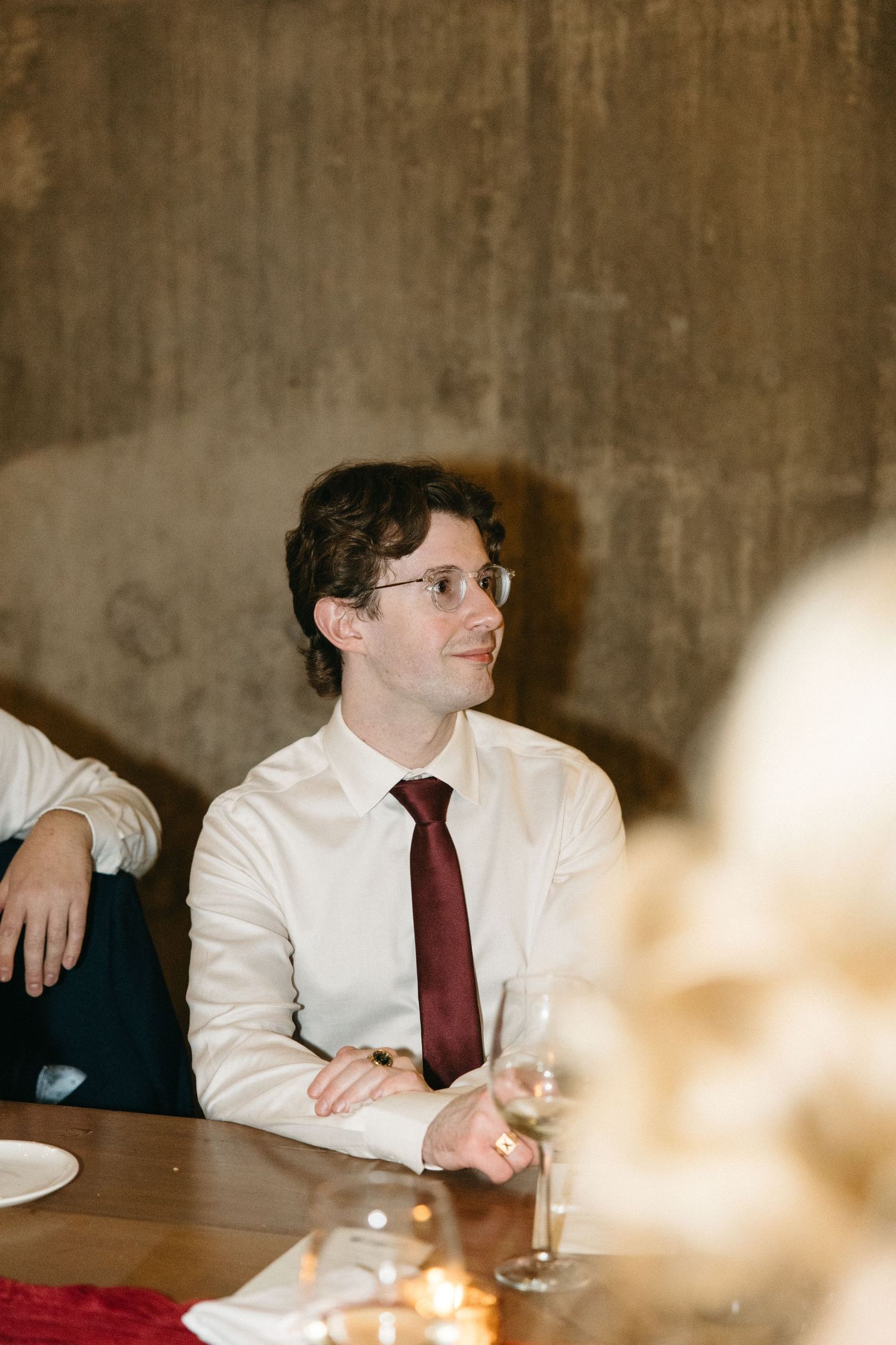 Guests in formal attire seated at a dimly lit dining table with candlelight.
