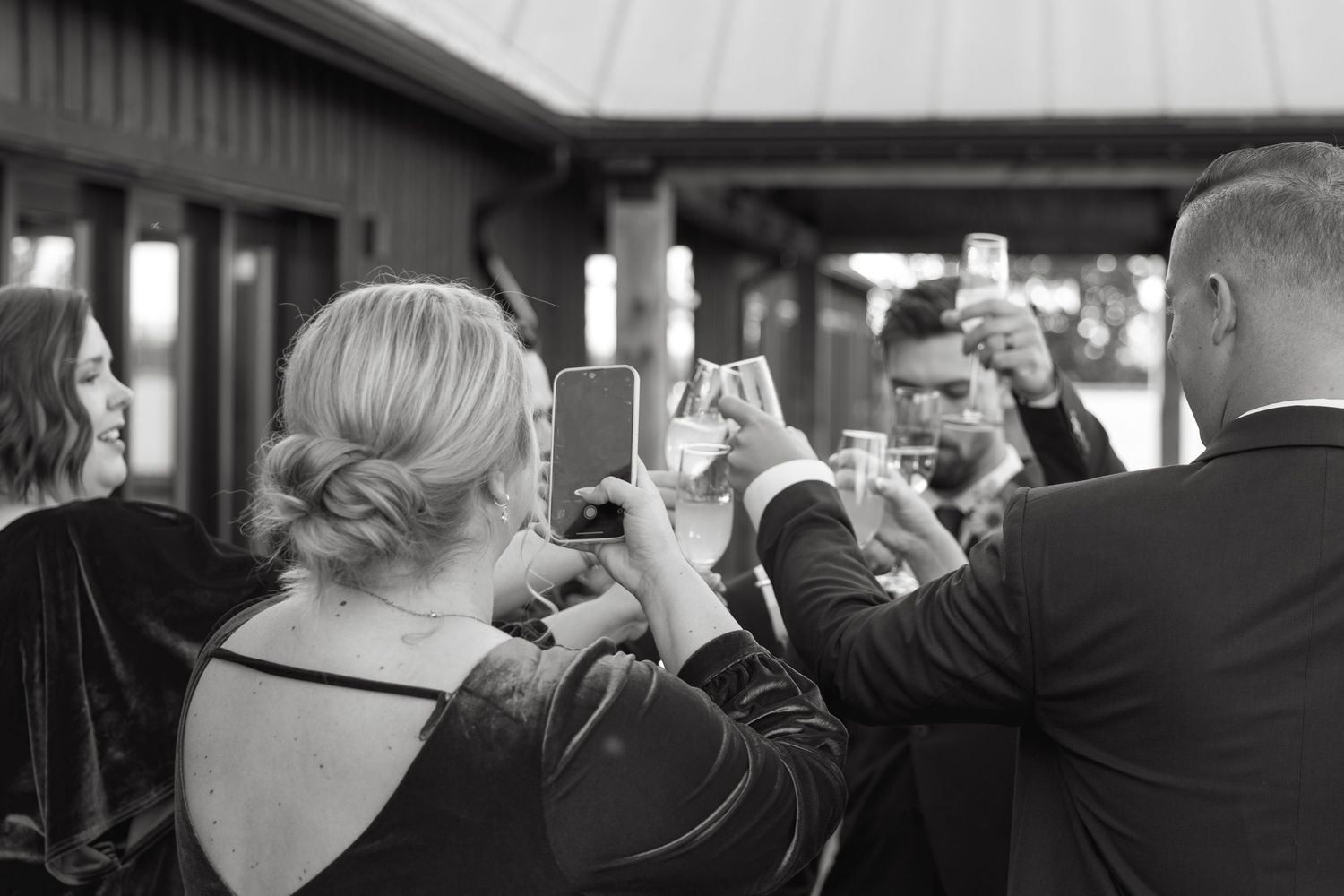 Wedding party members stand in a line outside a modern barn-style building.