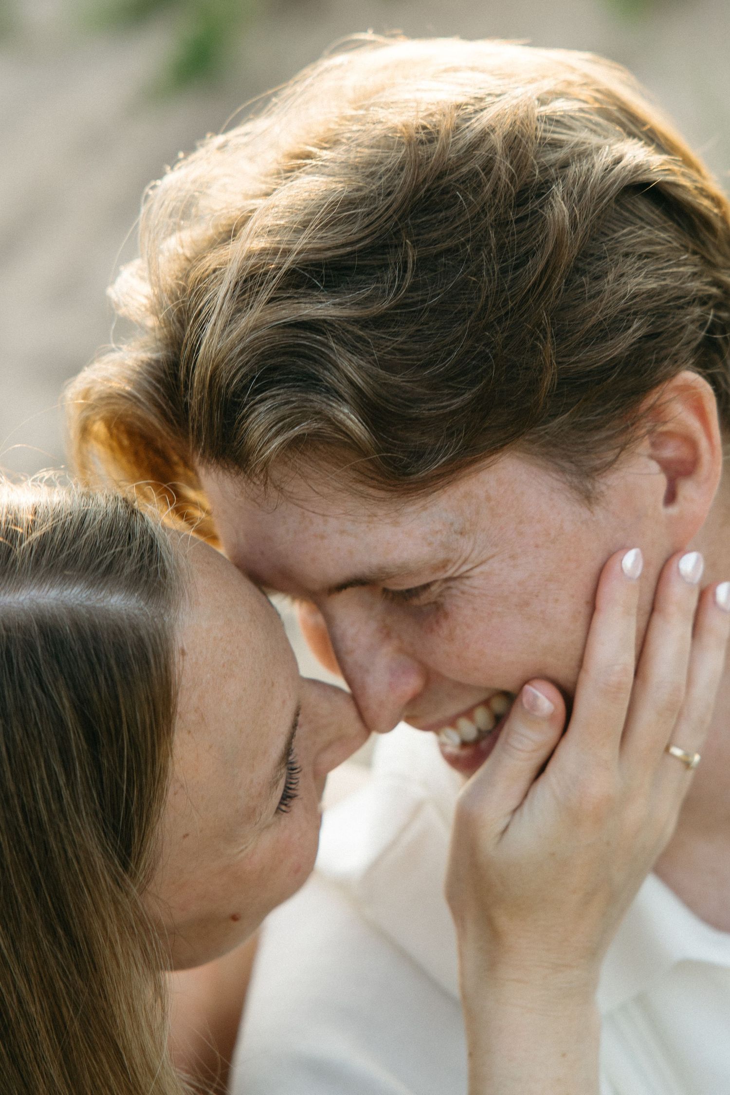 Joyful couple sharing an intimate moment, woman tenderly cradling mans face while both laugh.