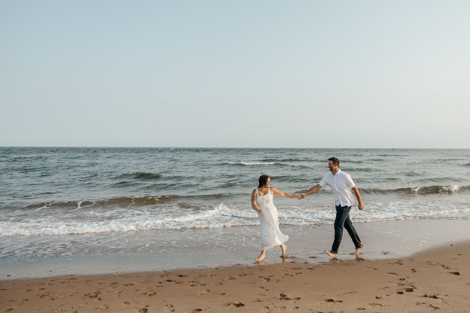 Two people walk and dance together on an empty beach by the ocean.